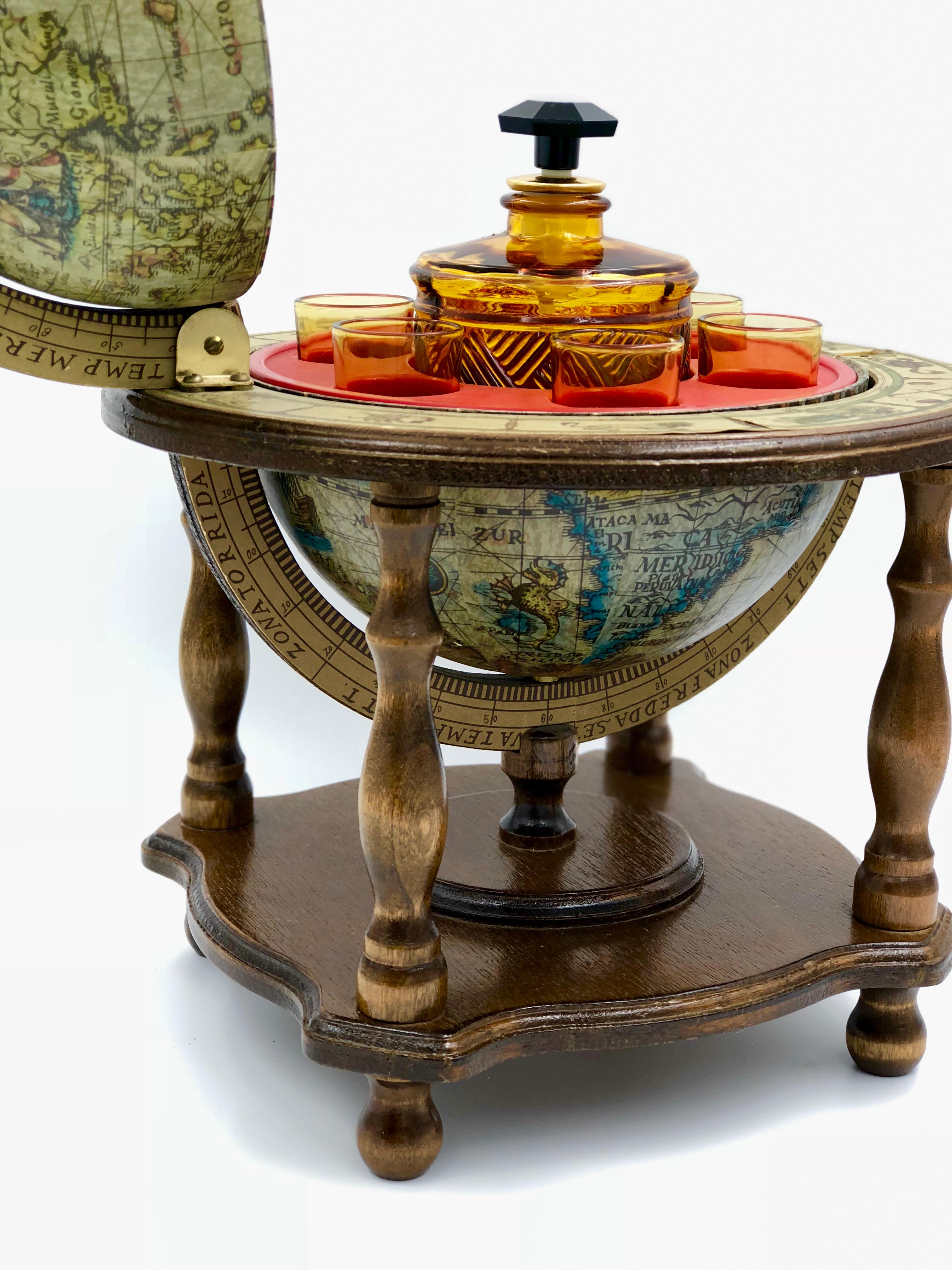 20th century spinning globe on a wooden platform base with turned legs. The globe opens to reveal an inner compartment containing an amber colored decanter and six matching cordial glasses.