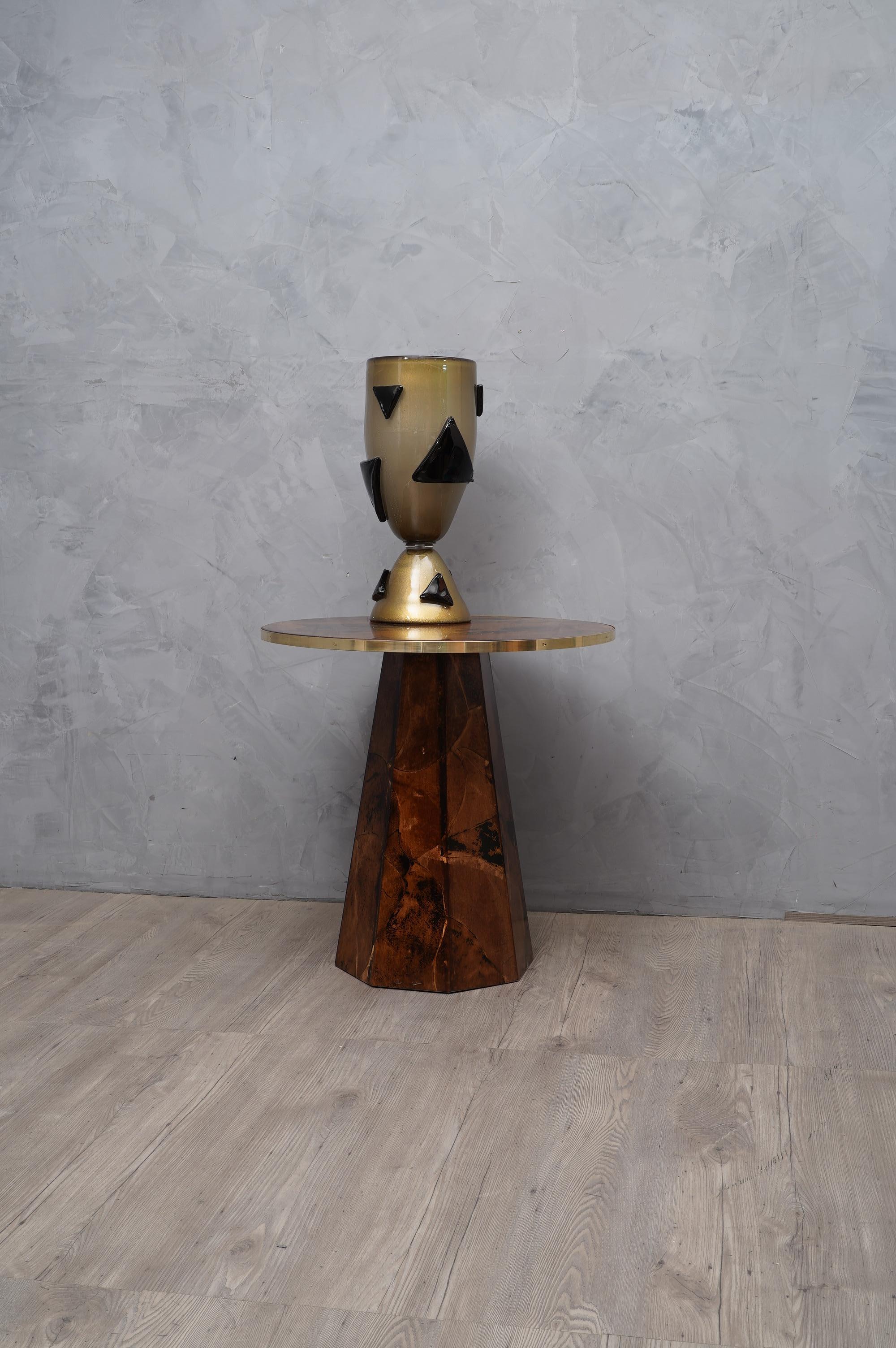 Side table out both for their elegance and essential linearity.

The side table have a wooden structure and is covered in colored and then resinated goatskin; the top is round in shape and has a brass edging, fixed with screws embedded in it. Its