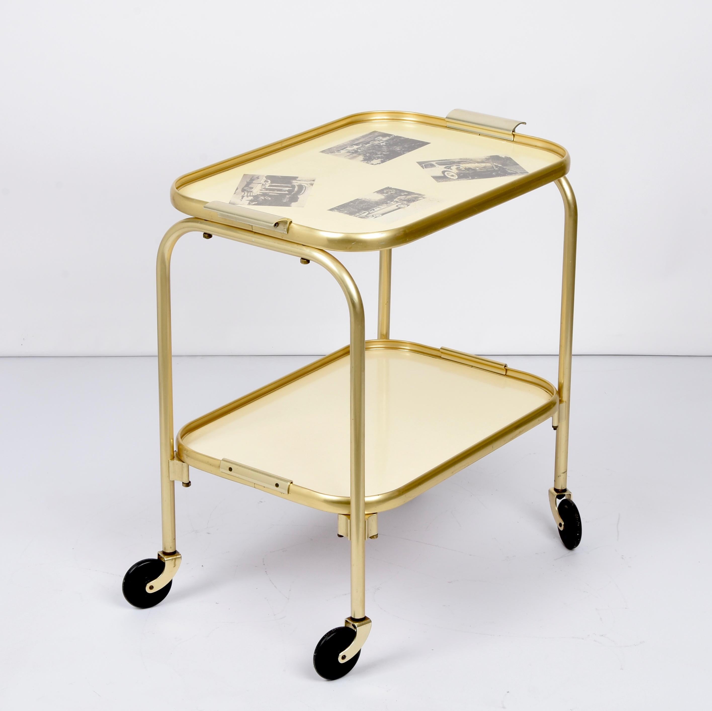 Carrito vintage único de aluminio dorado y formica de mediados de siglo. Este fantástico artículo se fabricó en Italia durante la década de 1950.

Una pieza preciosa con aluminio anodizado dorado y los estantes de fórmica amarilla dorada. La parte