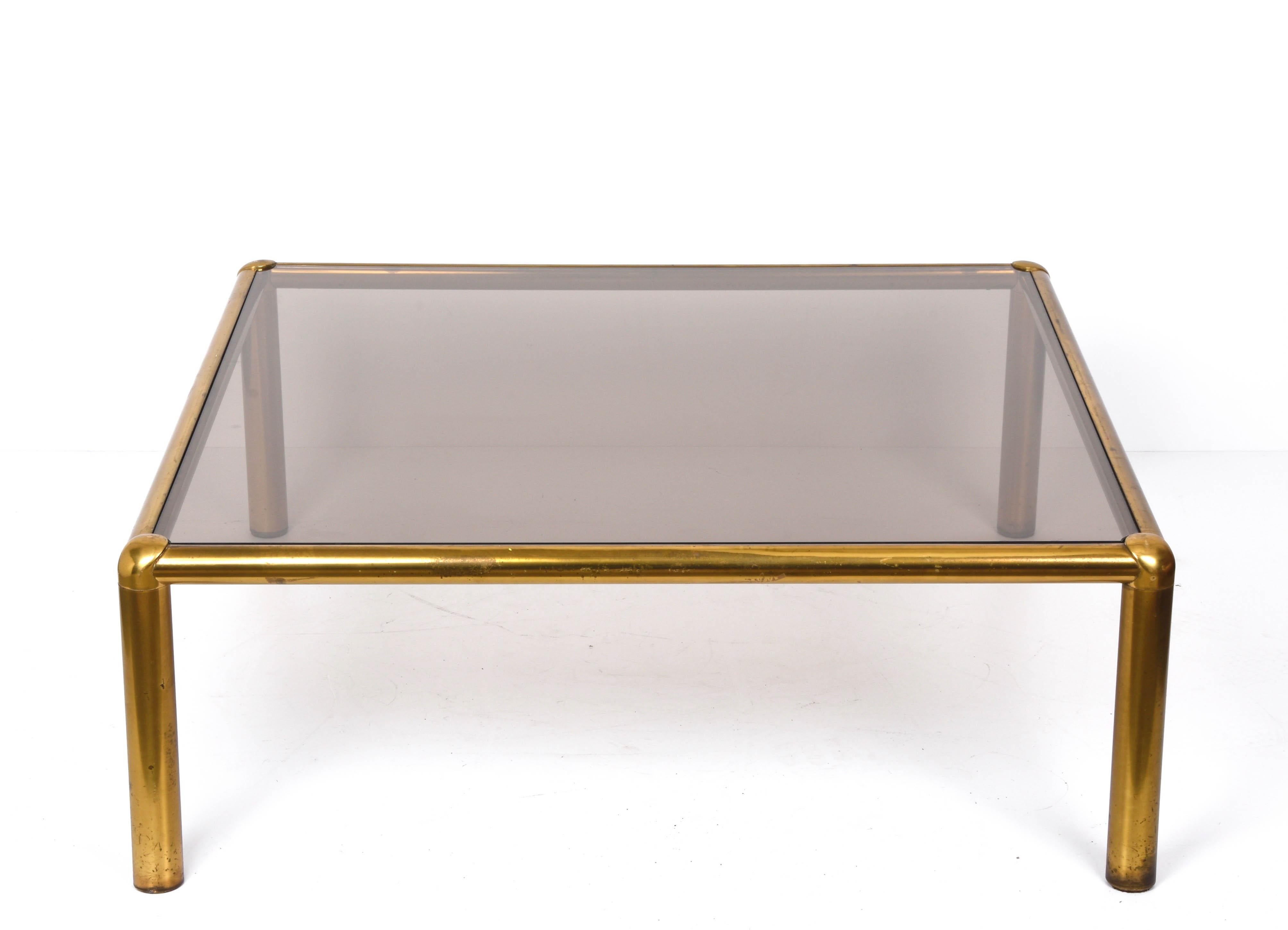 Amazing golden brass and smoked glass squared coffee table. This fantastic piece was designed in Italy during the 1980s.

This fantastic item has a wonderful top of smoked glass with delightful lines and a great material mix.

This item has some