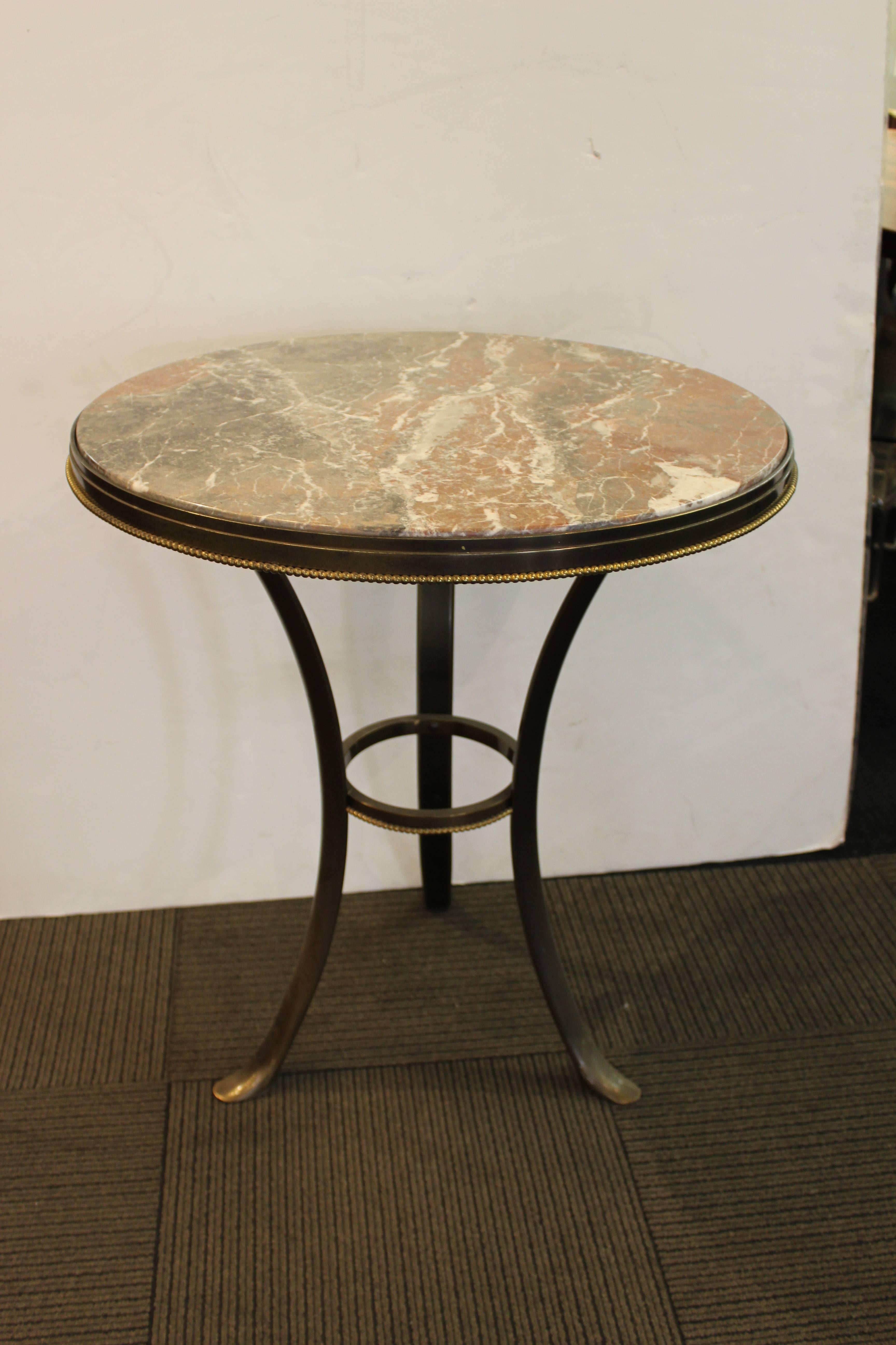 Gueridon table on three gently curved legs crafted in patinated bronze with a round marble top. Includes a decorative ring in between the table legs with gilt bronze 'beads' that mimic the pattern around the tabletop. Wear to brass finish on legs.