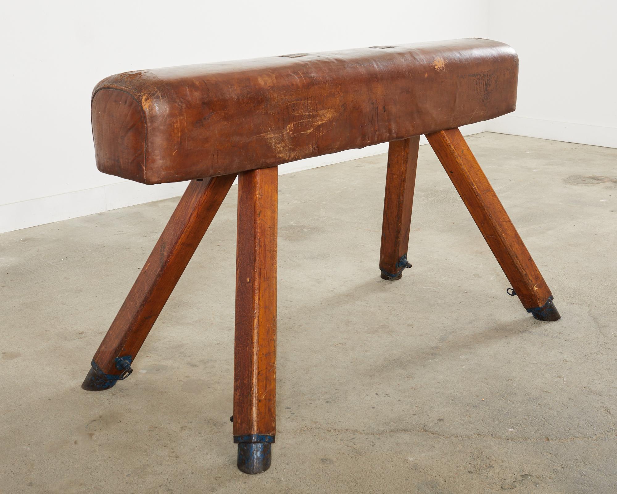 Large mid-century modern gymnastic pommel horse or bench vault. The bench features an oak frame covered with rich patinated cognac leather. The leather has a lovely aged patina with old repairs adding to its charm and character. The canted oak legs