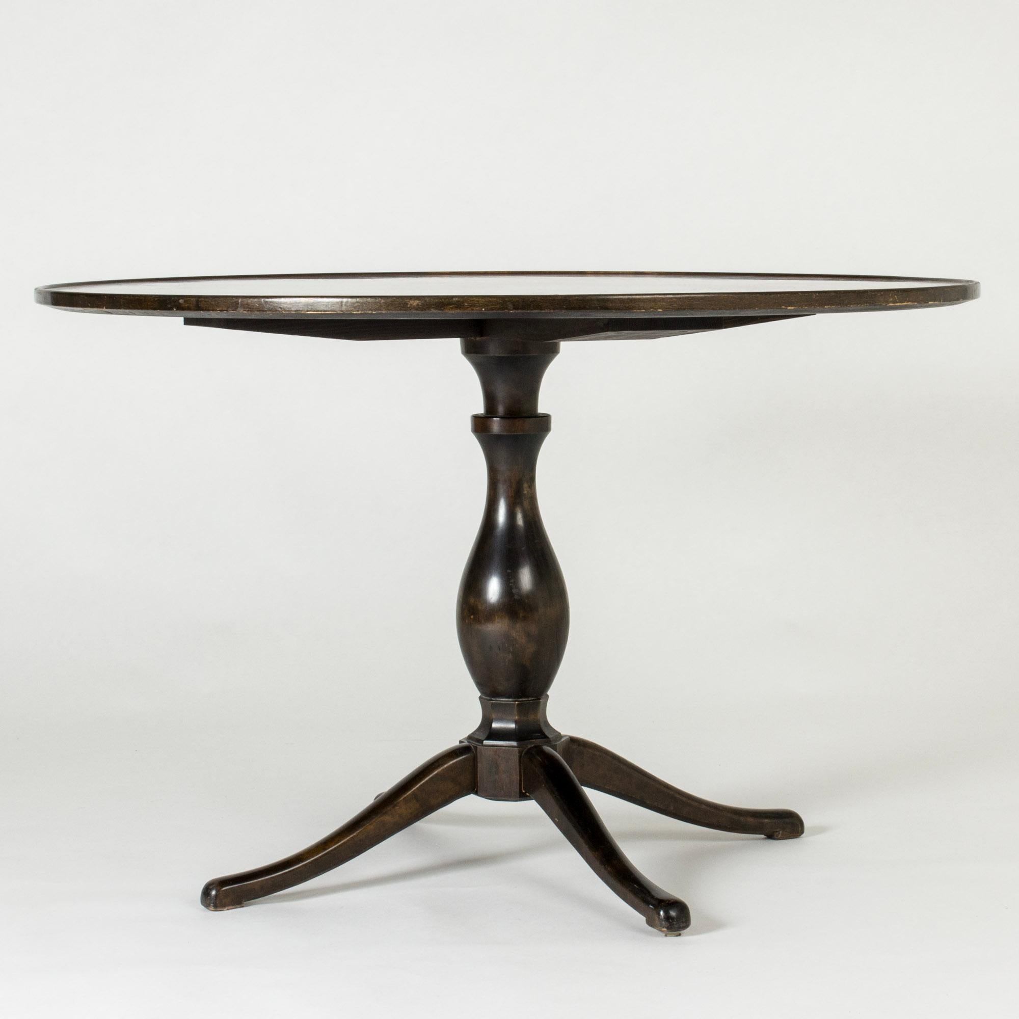 Elegant “Haga” dining table by Carl Malmsten, with a curvesome stained wooden base. Round table top with warm mahogany veneer in a checkered pattern.