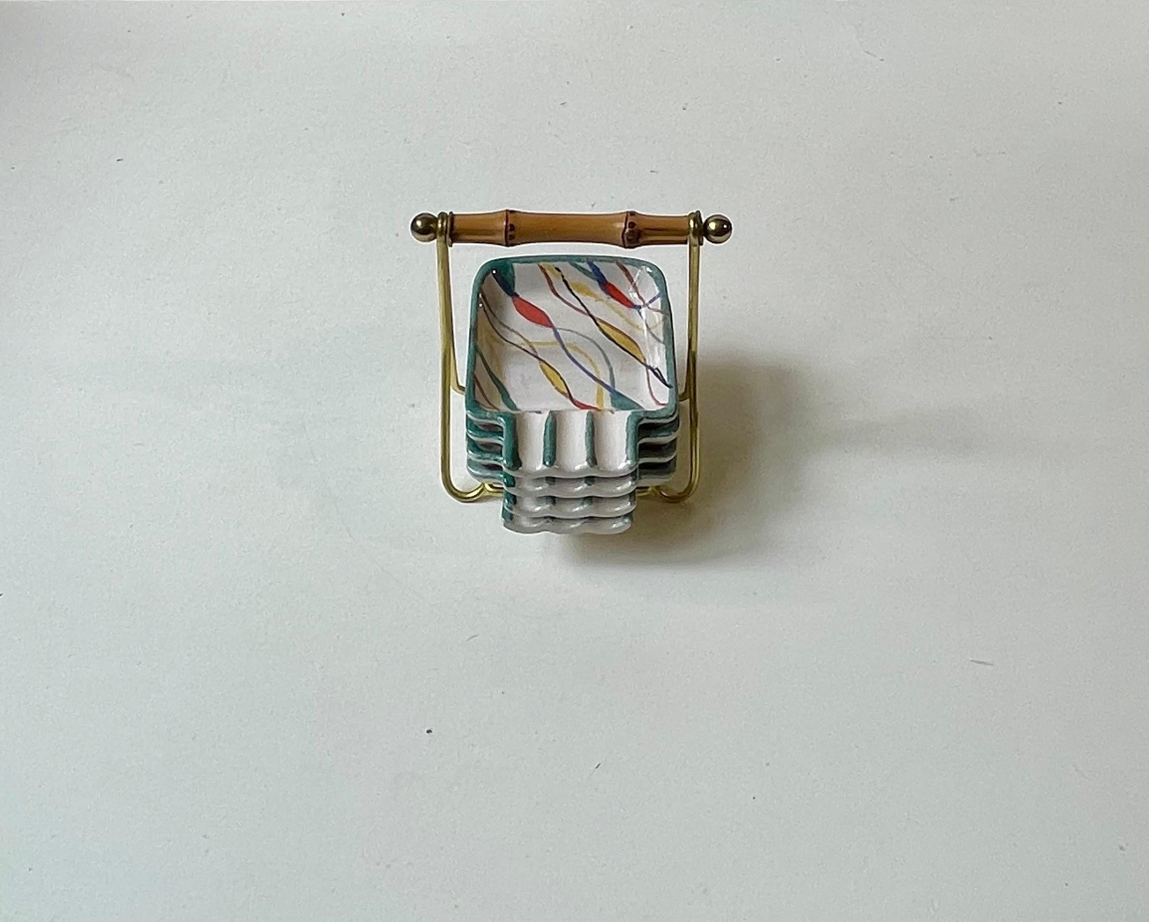 Cendrier en céramique peint à la main. Un ensemble de 4 dans un support élégant en bam-boo et en alliage de laiton. Décoration colorée atomique exécutée à la main. Fabriqué par üebelacker Keramik en Allemagne vers les années 1960. 

Dimensions :