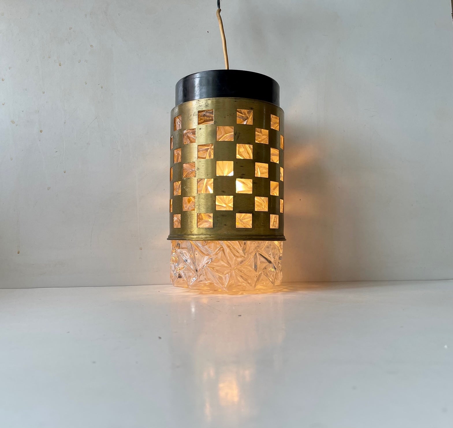 Midcentury modern German pendant ceiling light composed of pressed glass featuring a solid brass outer-shade with quadratic perforations. It was made at Bünte & Remmler - BuR Leutschen in Germany circa 1960. Measurements: H: 32 cm, diameter: 16 cm.