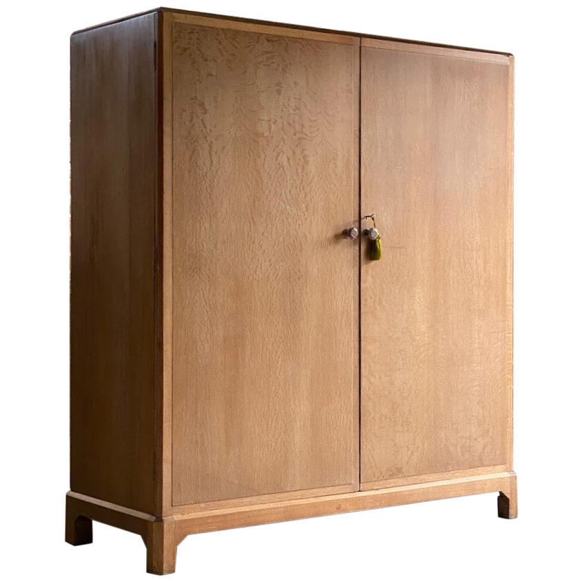 Magnificent early 20th century heal’s attributed limed oak two-door wardrobe compactum, England, circa 1930.

The rectangular top with canted corners over two figured, panelled solid oak doors with carved knob handles opening to reveal brass