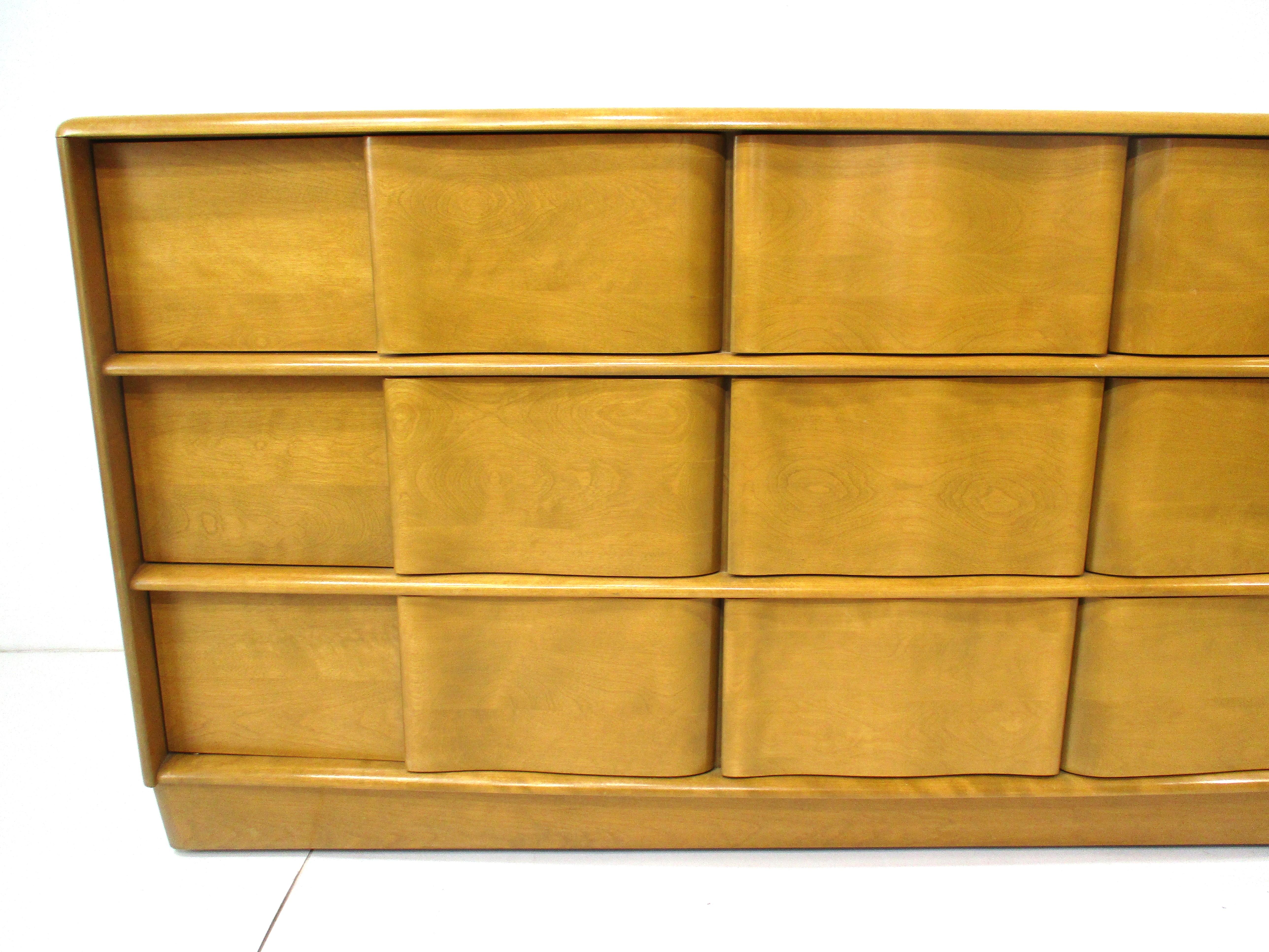 Un grande comò scultoreo del Mid Century a nove cassetti in legno massiccio d'acero Triplo con finitura color grano e molto spazio.  Disegnato da Leo Jiranek ed Ernest Herrmann per l'azienda di mobili Heywood Wakefield, questo pezzo appartiene
