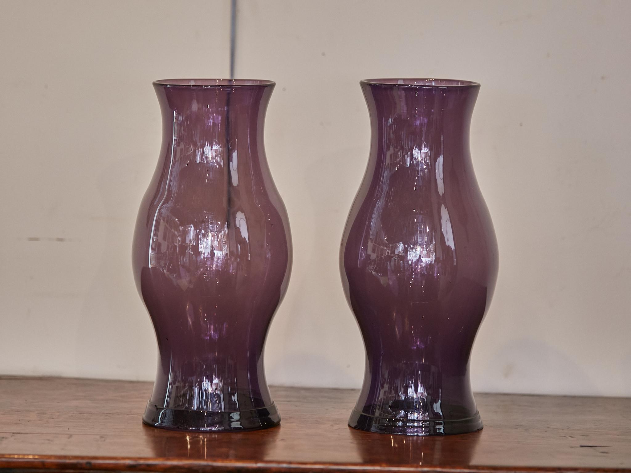 A pair of Midcentury American Amethyst color glass hurricane lamp shades. This pair of Midcentury American hurricane lamp shades, crafted in a radiant Amethyst hue, is a statement in both color and form. The deep, regal purple tone of the glass