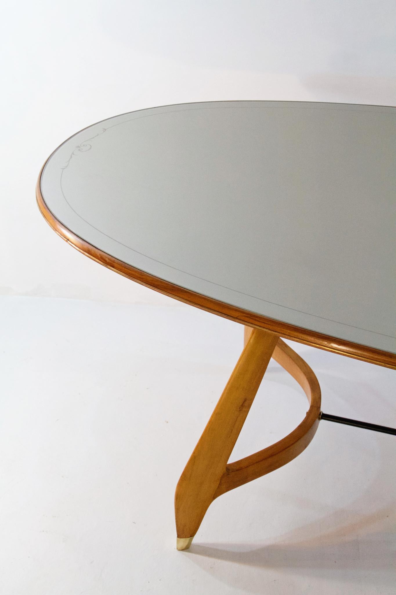 Fabulous oval dining table with an organic design and with a celadon green glass top with a decorative scroll border. Produced in Italy in the 1950s attributed to Augusto Romano. The legs have supreme craftsmanship are joined by a brass stretcher