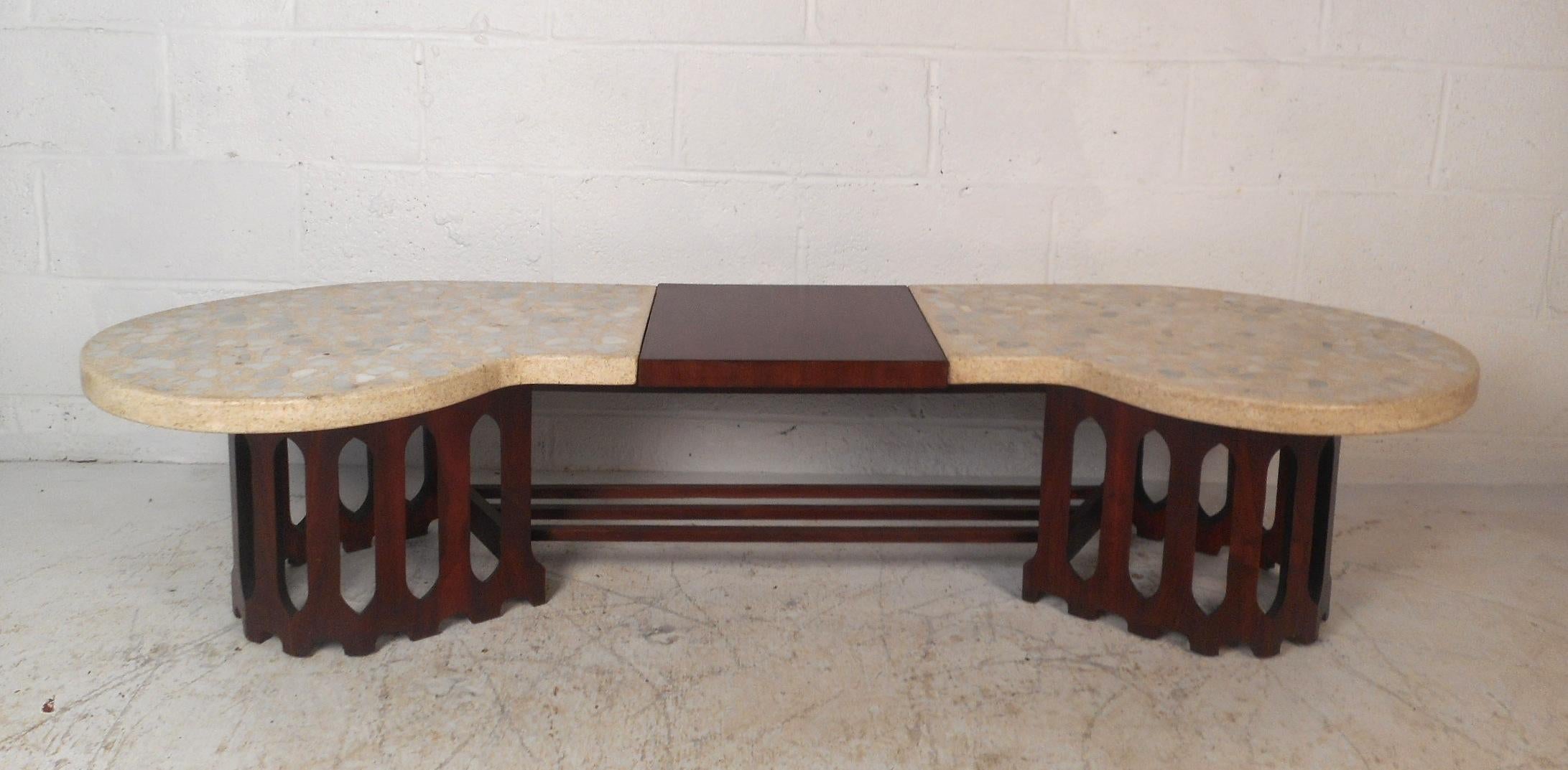 This beautiful Mid-Century Modern coffee table features an unusually shaped top and a sculpted base. A two-tone design with inlaid stones and walnut wood on the top. The sculpted base has three stretchers connected to each side for added sturdiness.