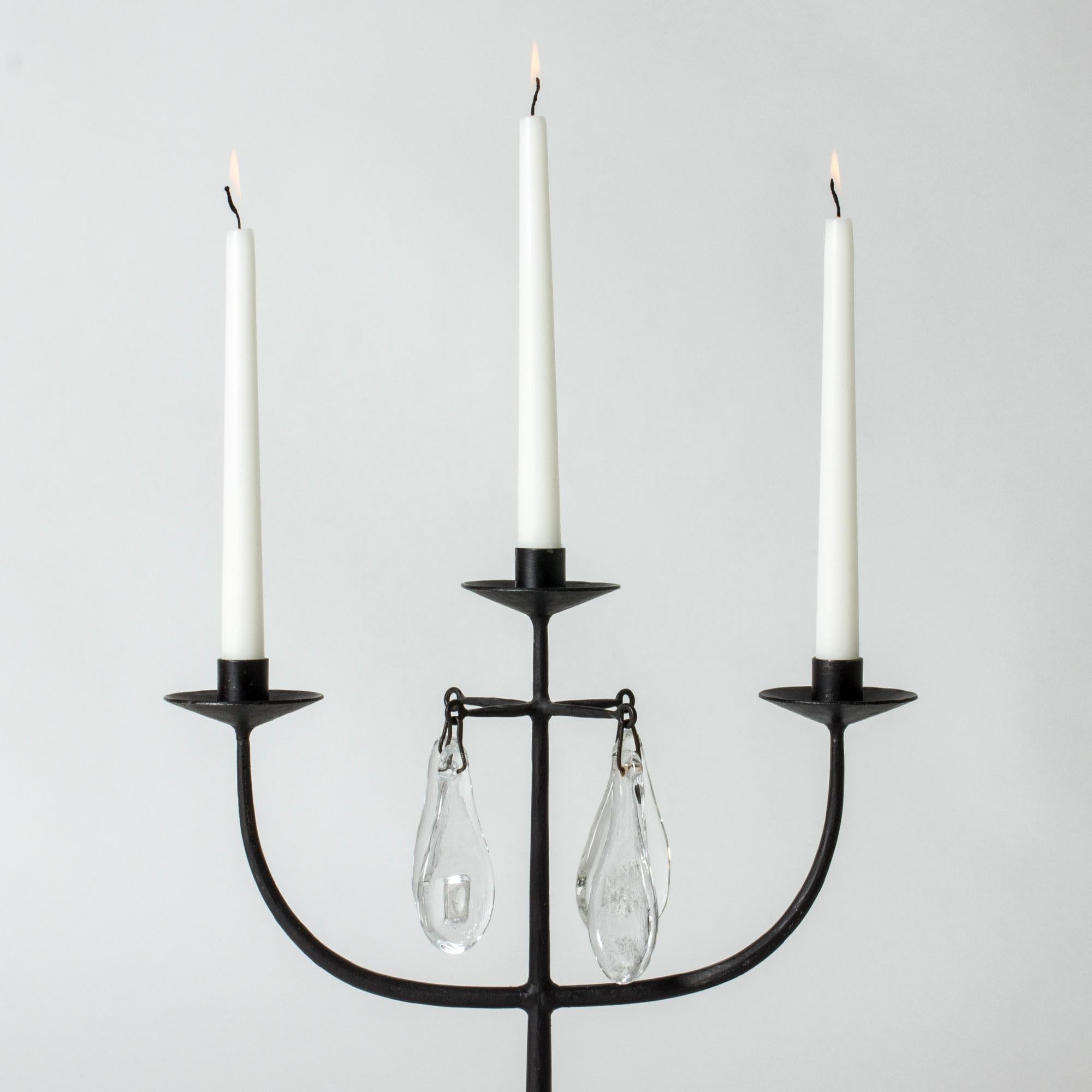 Beautiful candelabra by Erik Höglund, made from wrought iron and glass. The rustic iron stem is adorned with four pear shaped glass medallions that bring rain drops on a bare tree to mind. Fits regular candles.

Erik Höglund was one of Sweden’s