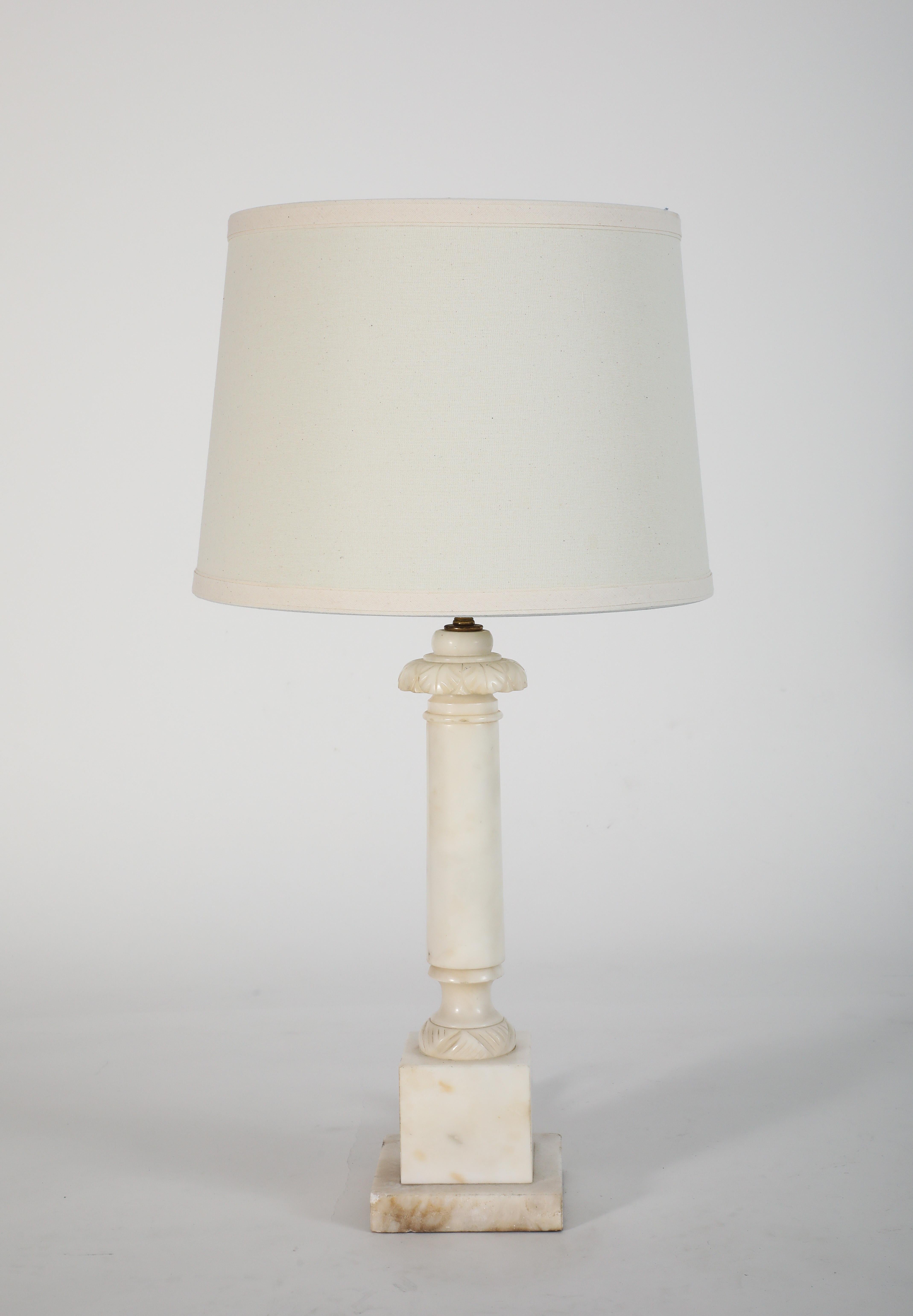 Vintage midcentury carved alabaster table lamp. The cylindrical columnar shaft is surmounted by a foliate-carved capital and raised on a stepped square base, fitted with a cream fabric shade. Exhibiting characteristic veining and translucence of