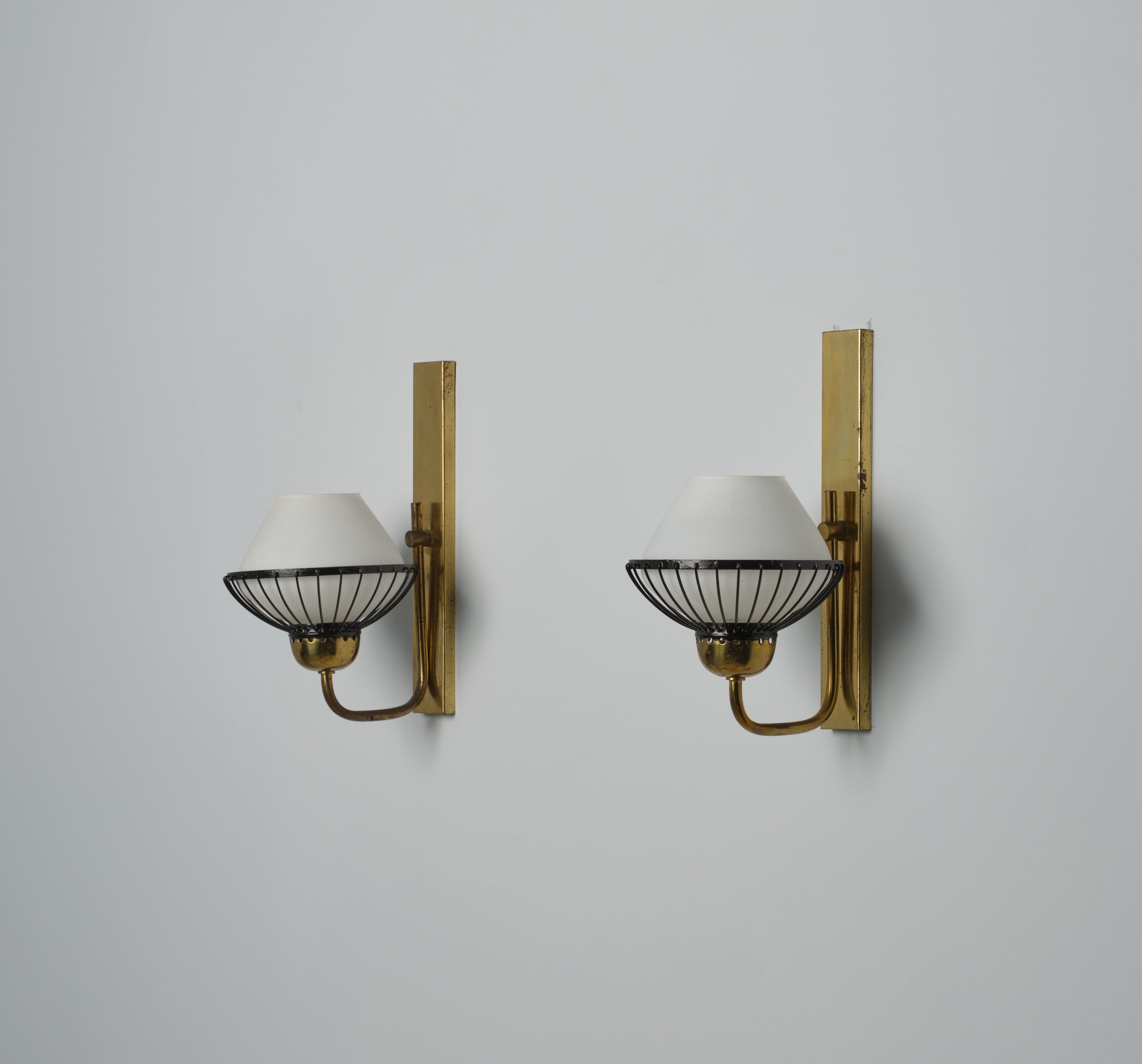 Pair of midcentury Italian wall lamps, known as appliques. Crafted in the 1950s, these pieces exude sophistication and refinement. Each lamp is meticulously fashioned from brass, featuring accents of black metal and opal glass lampshades. Despite