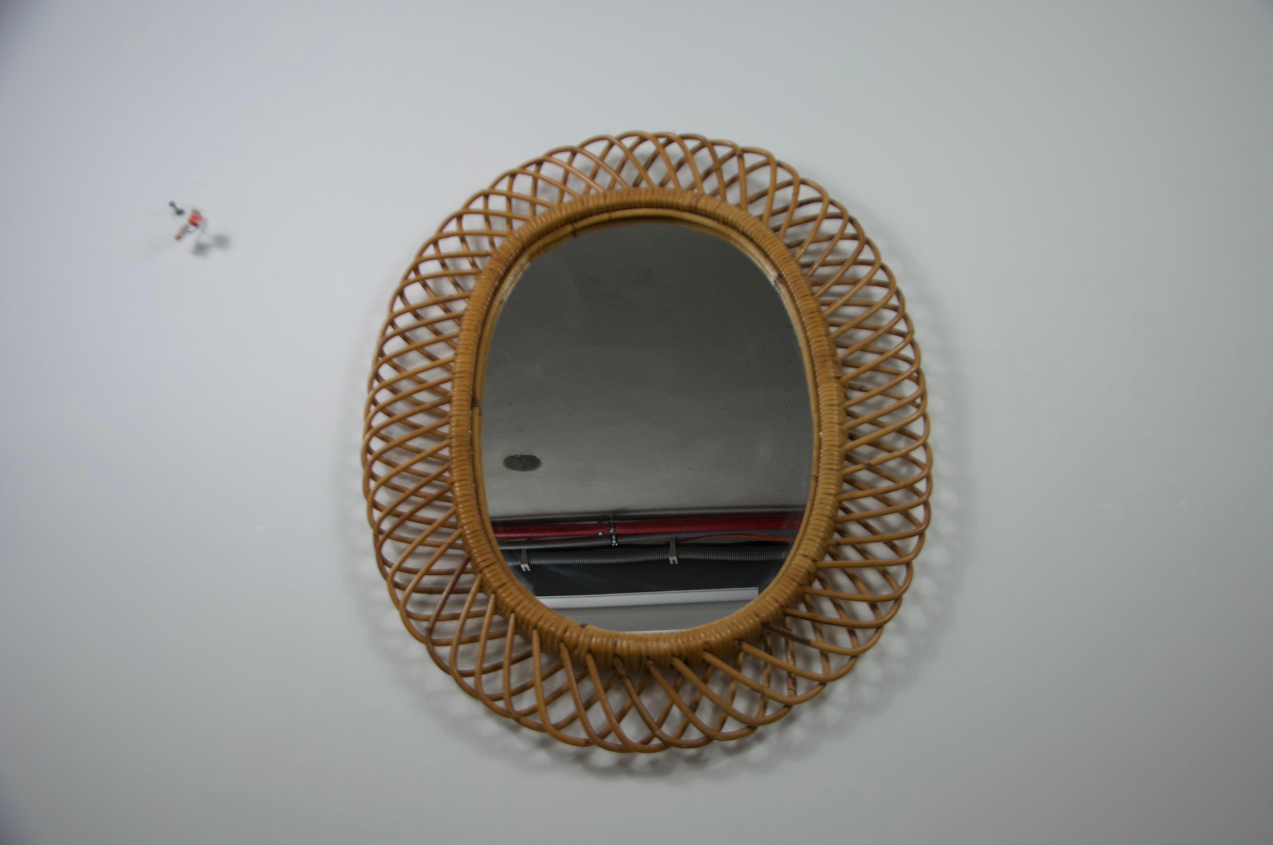 A charming midcentury wall mirror crafted in Italy during the 1960s, featuring a beautifully woven bamboo frame. The oval shape is accentuated by an intricate radial wicker design, embodying the natural elegance and organic warmth characteristic of