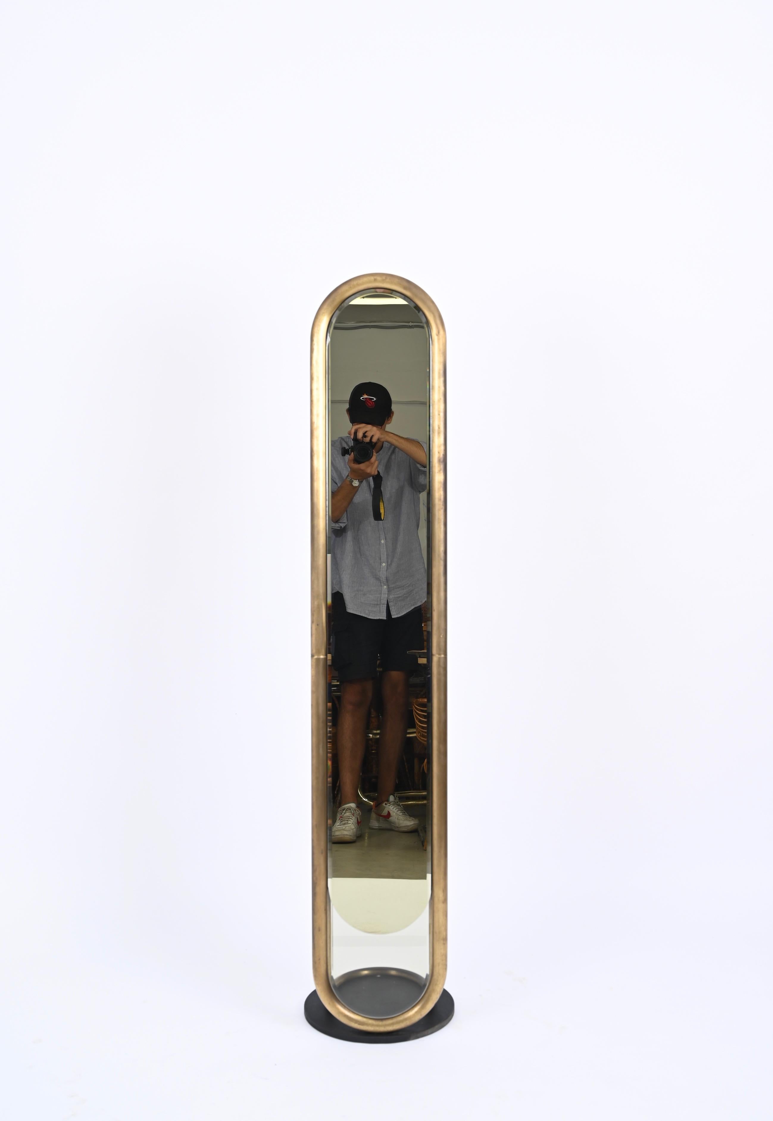Marvellous floor mirror in solid brass with bronze mirror and black enameled metal base. This unique piece was designed in Italy in the 1970s.

This gorgeous floor standing mirror has a stunning oblong beveled bronze mirror that ends on the bottom