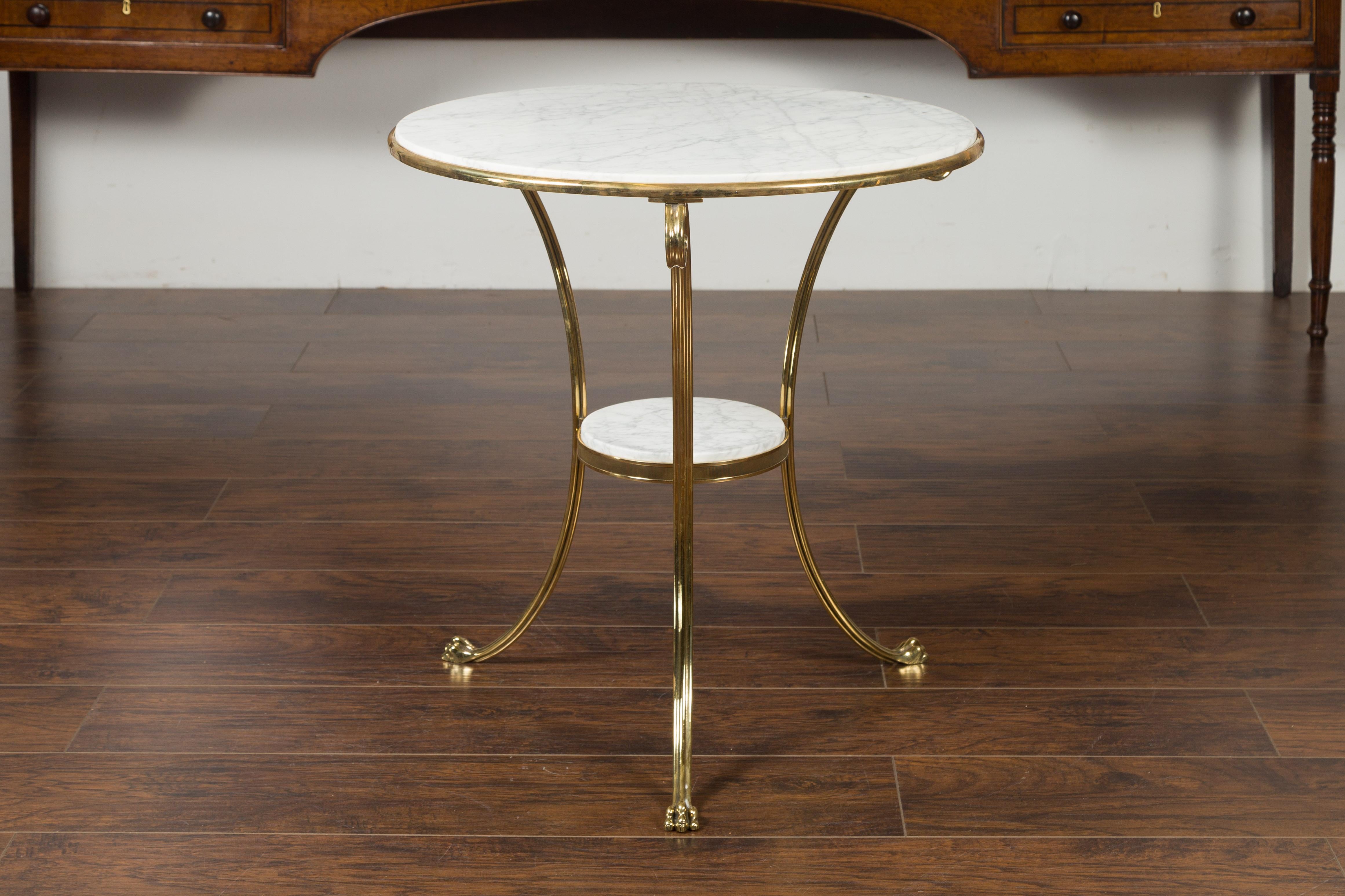 A vintage Italian brass side table from the mid-20th century with round marble top and shelf. Created in Italy during the midcentury period, this stylish side table features a circular white veined marble top secured within a brass structure. Three