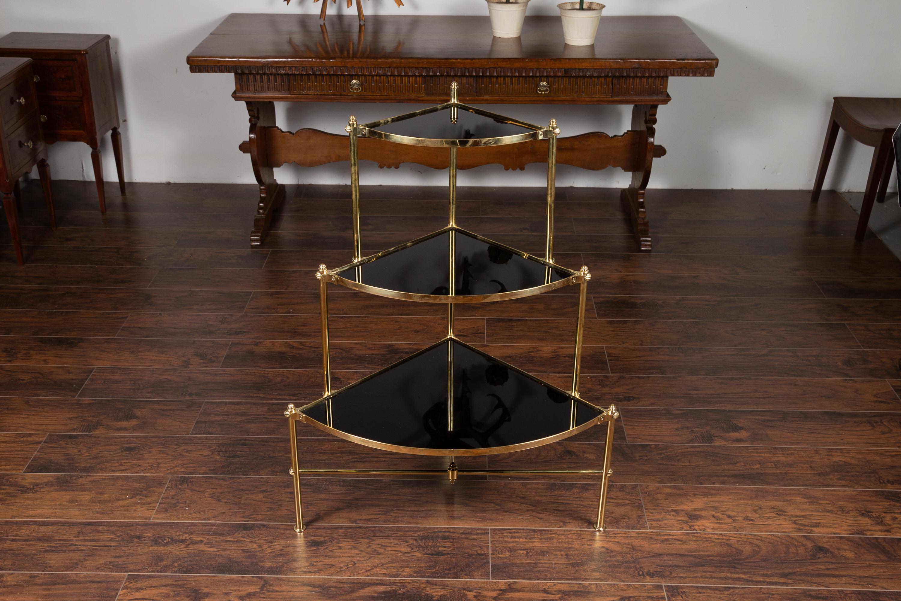 A vintage Italian tiered brass corner étagère from the mid-20th century, with black glass shelves. Born in Italy during the midcentury period, this stylish corner étagère features an elegant brass structure strengthened with stretchers, securing