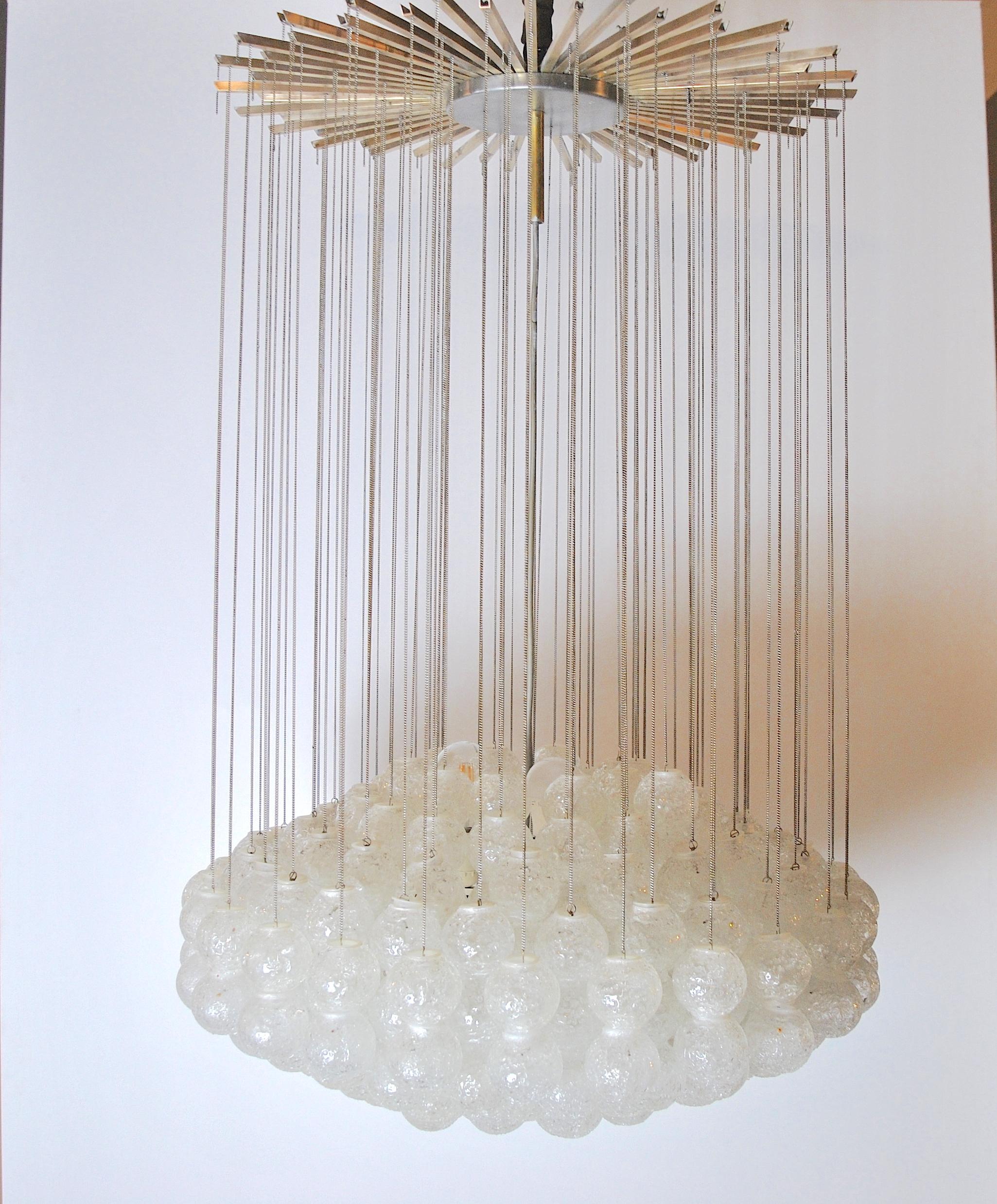 Exclusive midcentury Italian chandelier after Zero Quattro made of Murano Glass spheres hanging hanging on brass chains from a brass star shaped canopy. Light bulbs are located at the same height of the spheres therefore they perfectly mix with them