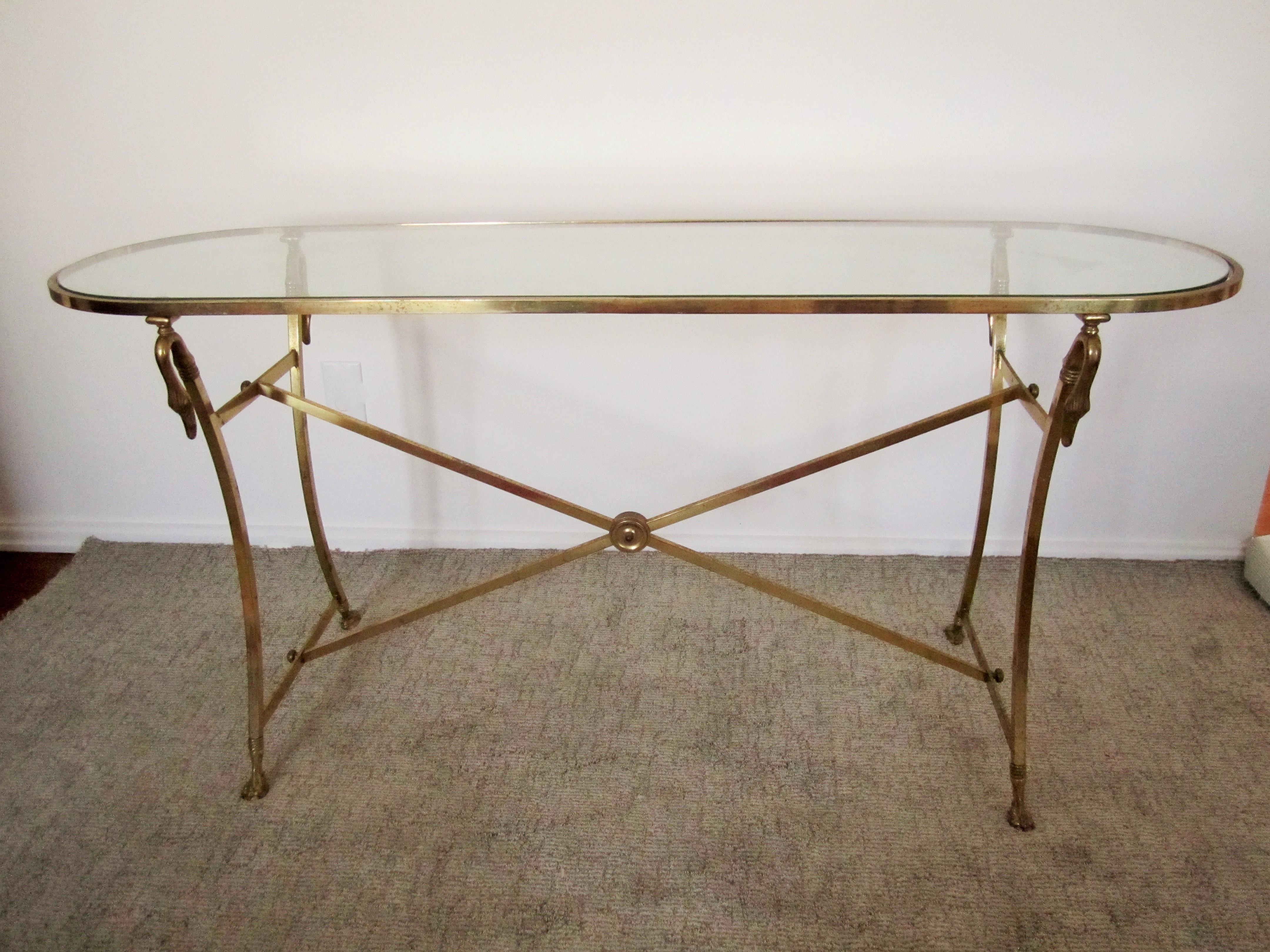 A Regency style Italian or French console table in brass and glass, circa mid-20th century. Consoles' brass base has swan head and neck detailing at top, ball and claw feet at base, with stretcher in-between, and an 'inset' glass top. Console has