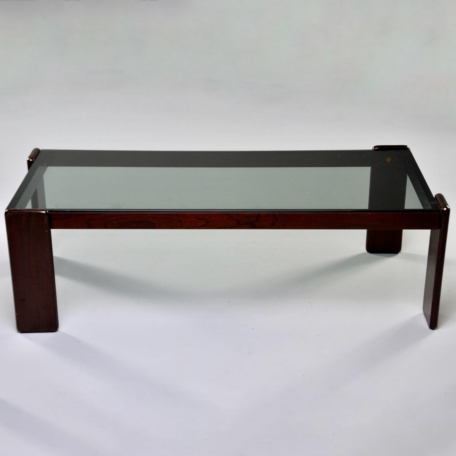 Italian cocktail table has a dark stained wood frame with smoke colored glass top, circa 1970s. Flat, rectangular legs are oriented with one affixed to each short side one on each long side to add visual interest. Unknown maker. 

Glass Only: 47.25”