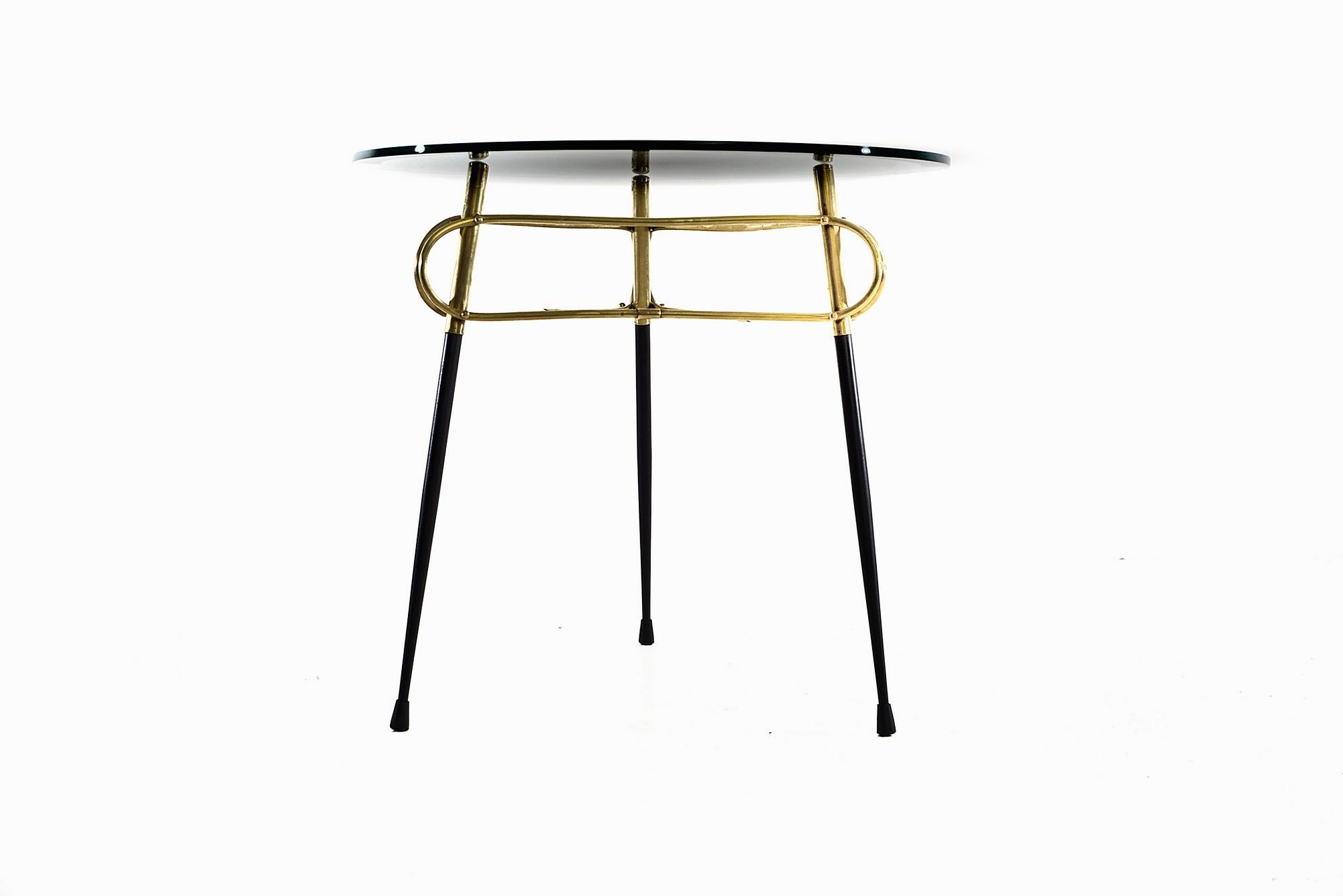 This three legged coffee/cocktail table has a round table top with beveled edges it is resting on a triangular frame in black steel and brass.