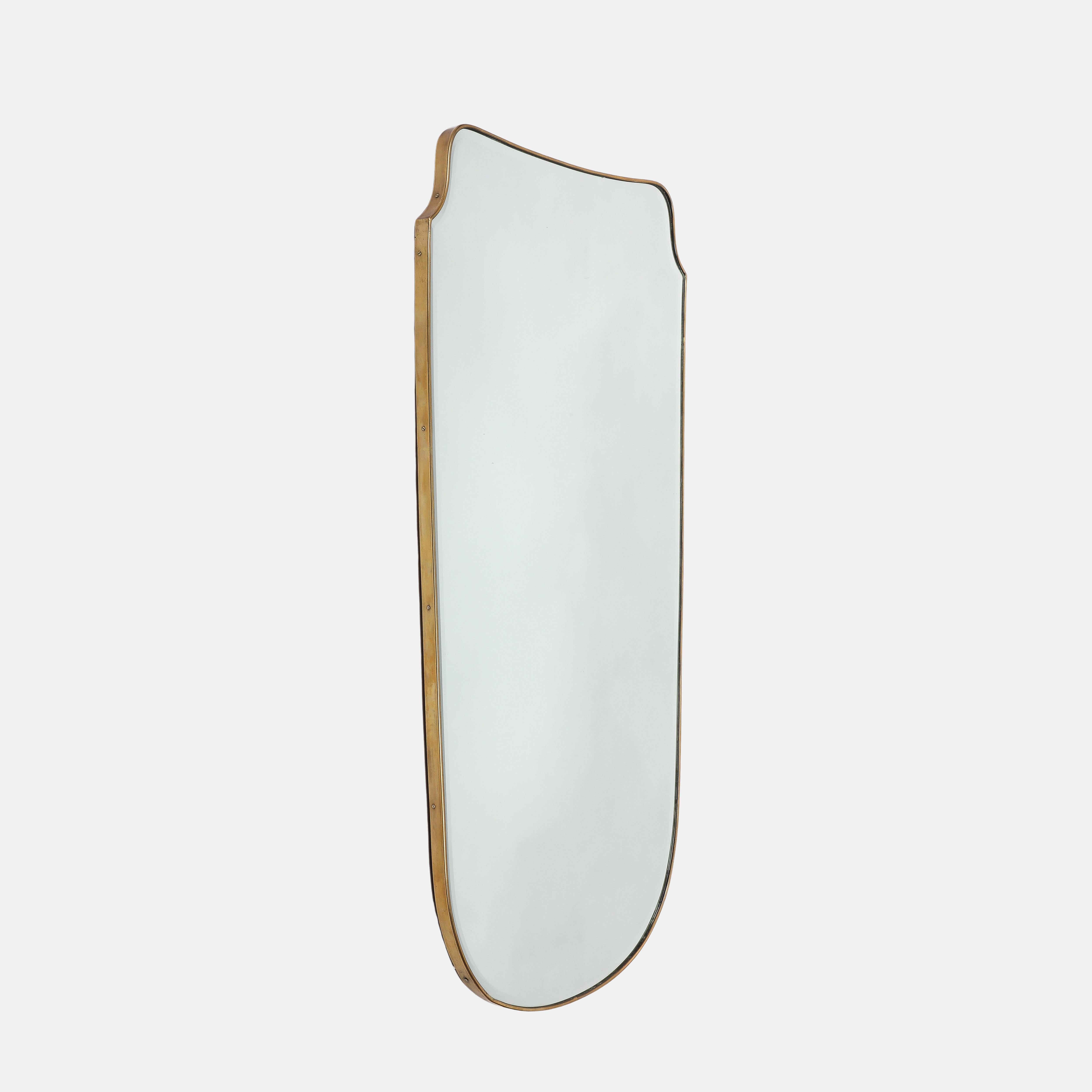 Midcentury Italian exquisite grand scale shield shaped brass beveled mirror with wood backing and lined with felt, 1950s. This original midcentury period mirror has a beautiful rich patina to the brass, elegant soft curves, and gently tapering