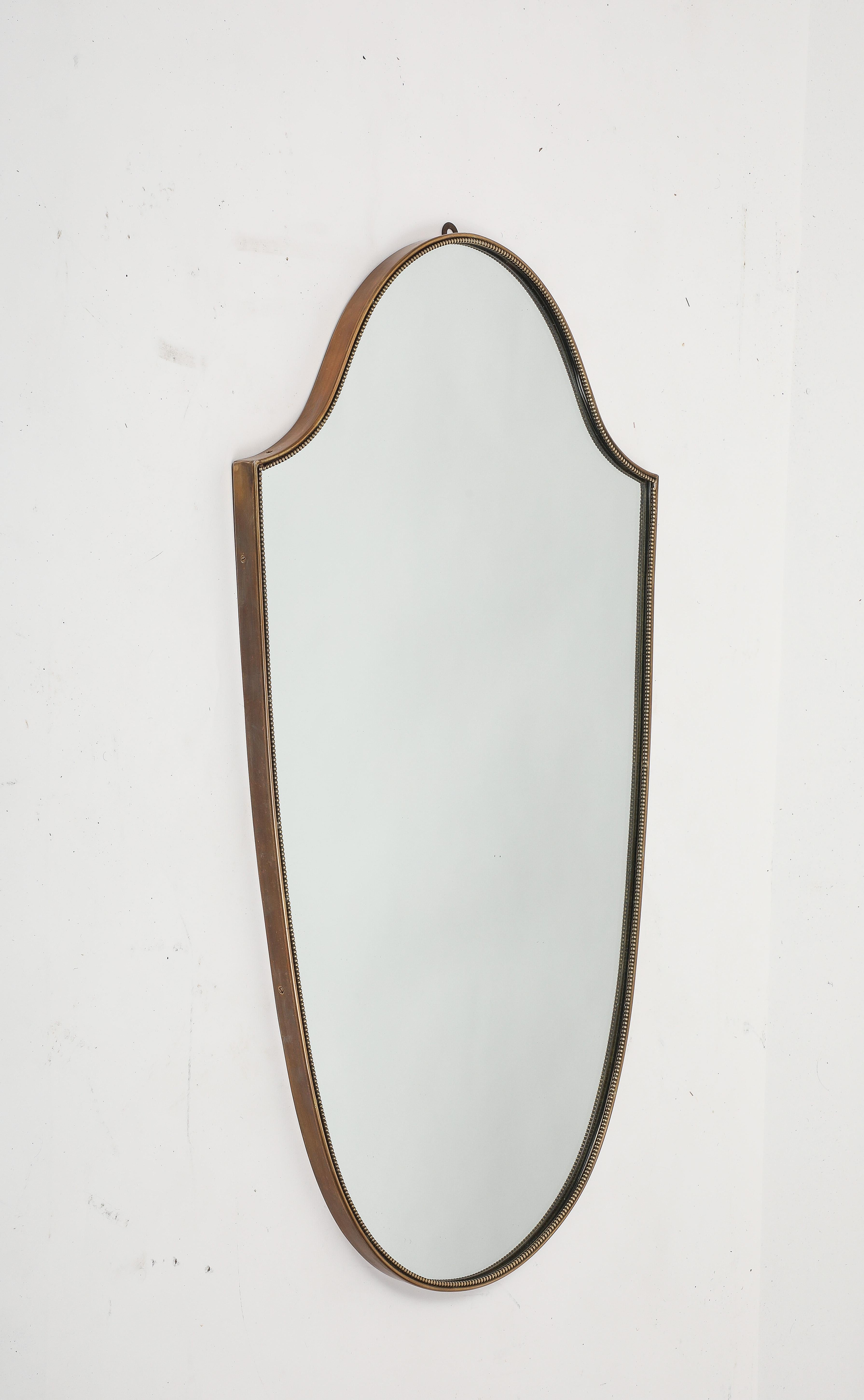 Italienischer eleganter schildförmiger Wandspiegel aus Messing mit Perlen, 1950er Jahre. Dieser originale Spiegel aus der Mitte des Jahrhunderts hat eine schöne geschwungene Form und eine schöne reiche Patina auf dem Messing.