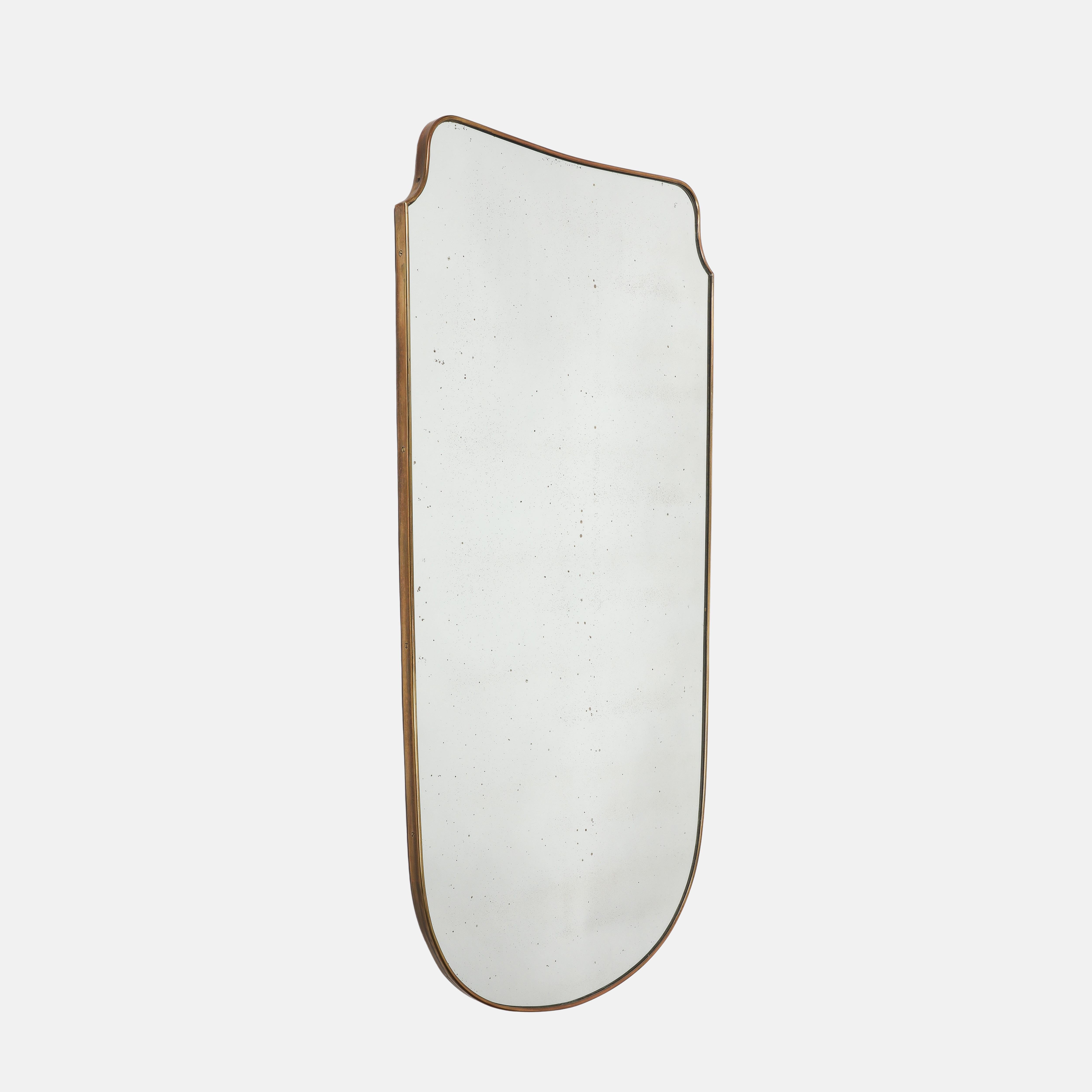 Italienischer, exquisiter, schildförmiger Messingspiegel aus der Jahrhundertmitte mit Holzrückwand, 1950er Jahre. Dieser originale Spiegel aus der Mitte des Jahrhunderts hat eine schöne, reiche Patina auf dem Messing, elegante, weiche Kurven und