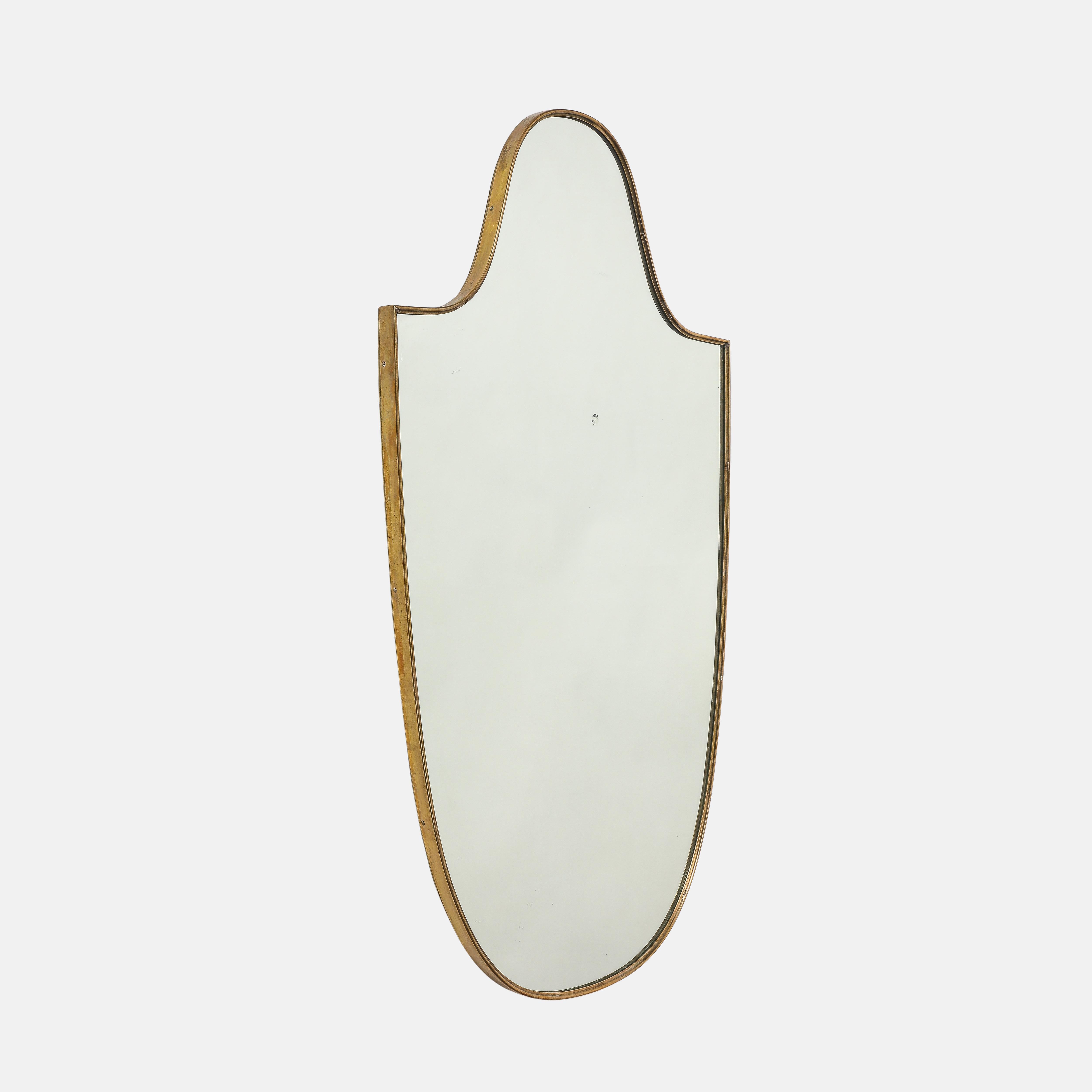 Elegant miroir mural italien en laiton en forme de bouclier, années 1950.  Ce miroir original de la période du milieu du siècle a une belle forme incurvée et une belle patine riche au laiton.