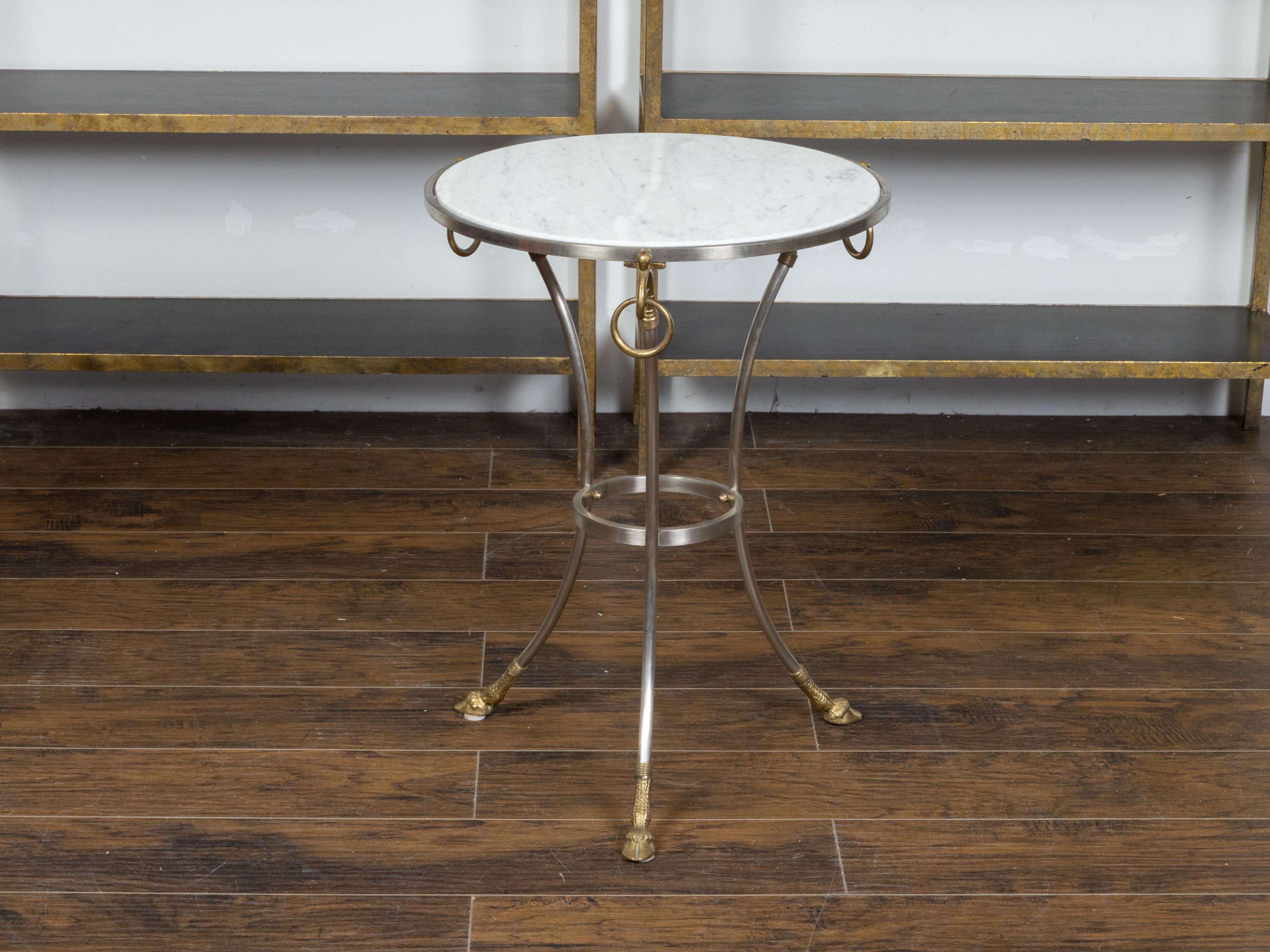 A vintage Italian Maison Jansen style steel and brass side table from the mid 20th century with white veined round shaped marble top, ring pulls, lower ring and hoof feet. Created in Italy during the Midcentury Modern period, this Maison Jansen