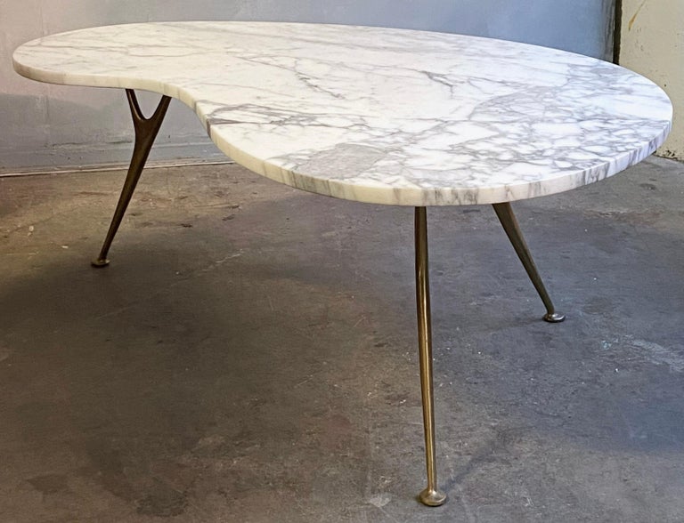 Beautiful ameba / biomorphic kidney shaped marble coffee table with solid brass splayed legs. Featuring striking wishbone style legs mounted under a marble top. The legs are fixed to a wood surface hidden under the bottom of the marble top making it