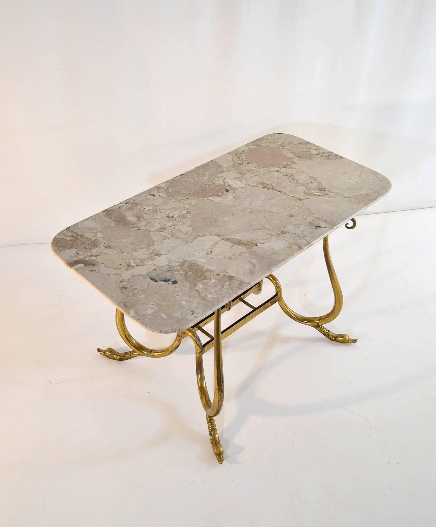 Elegant cocktail table with a sweeping design in the base in brass with swan feet and a top in a neutral beige marble. Designed and produced sometime during the 1950s.