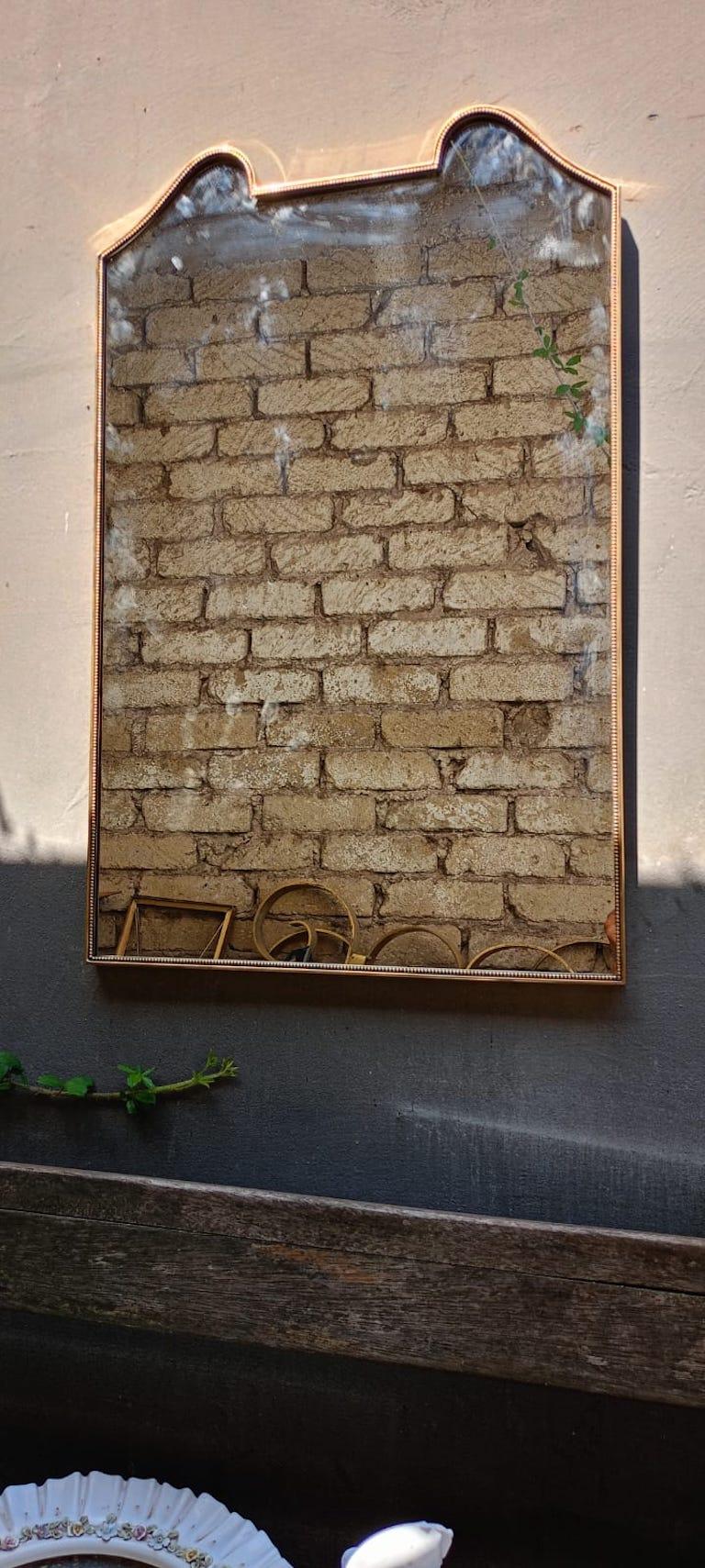 Miroir mural italien du milieu du siècle, avec un cadre en laiton poli au design élégant dans la partie supérieure. Cadre/profil décoré avec d'élégantes perles le long du bord