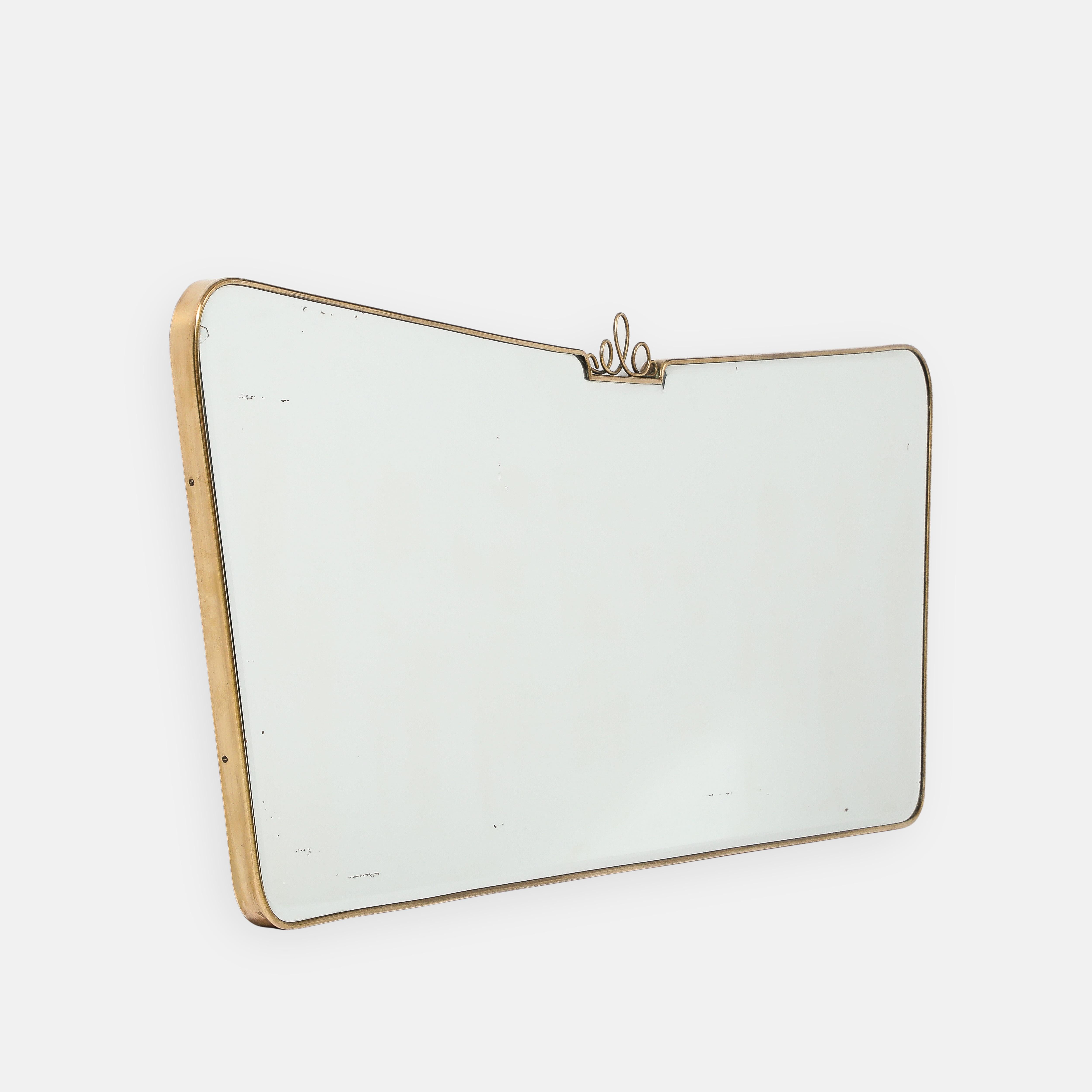1950s Italian modernist horizontal overmantel brass mirror in the style of Gio Ponti.  This exquisite original beveled glass mirror has a gently curved brass frame with rounded corners and gently tapering sides, central top decorative brass scroll