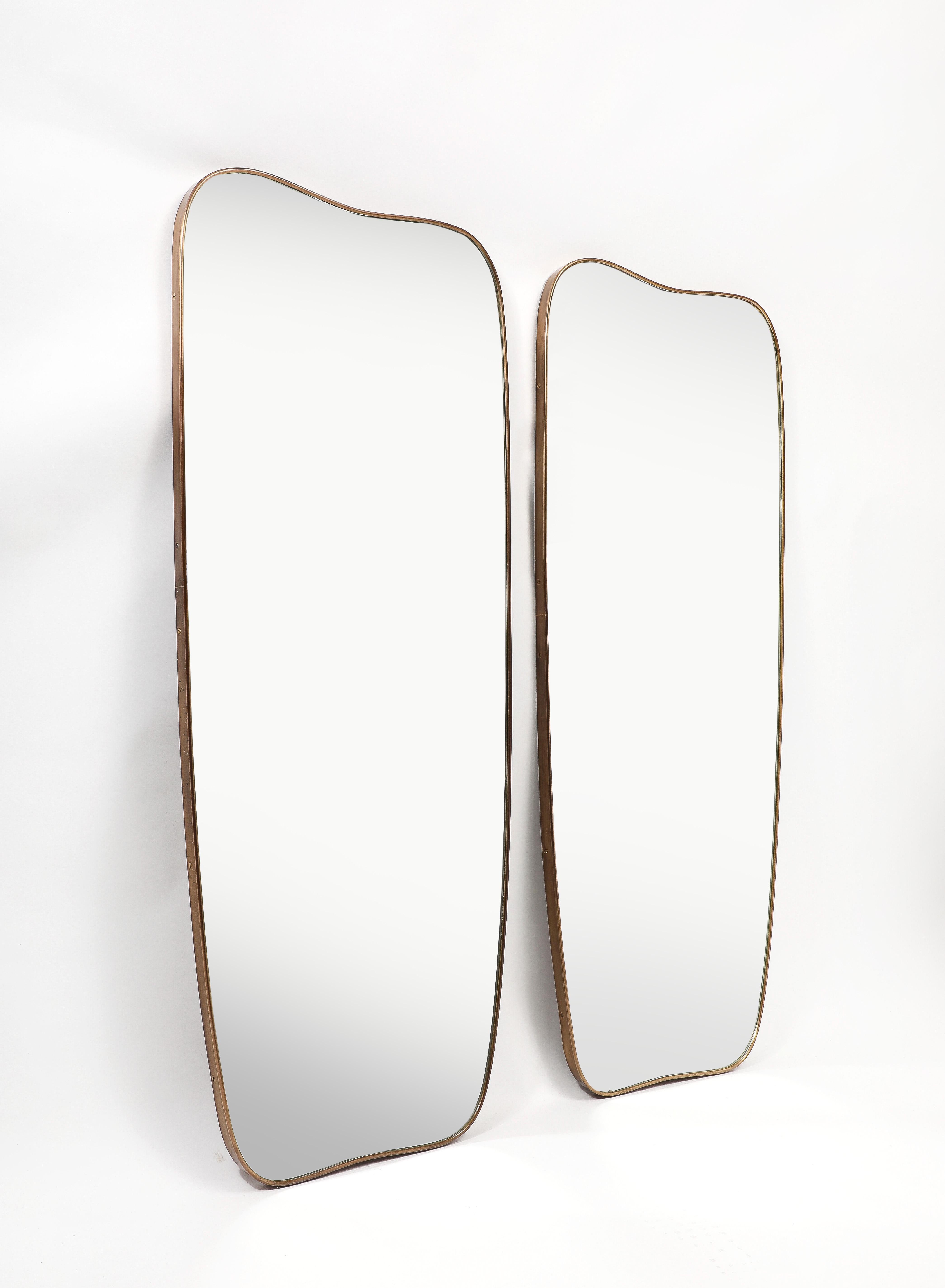 1950s Italian modernist pair of grand scale wall mirrors consisting of shaped brass frames with gently arched tops and bottoms with rounded corners which taper towards the bottom. These chic pair of mirrors are truly an iconic Italian midcentury