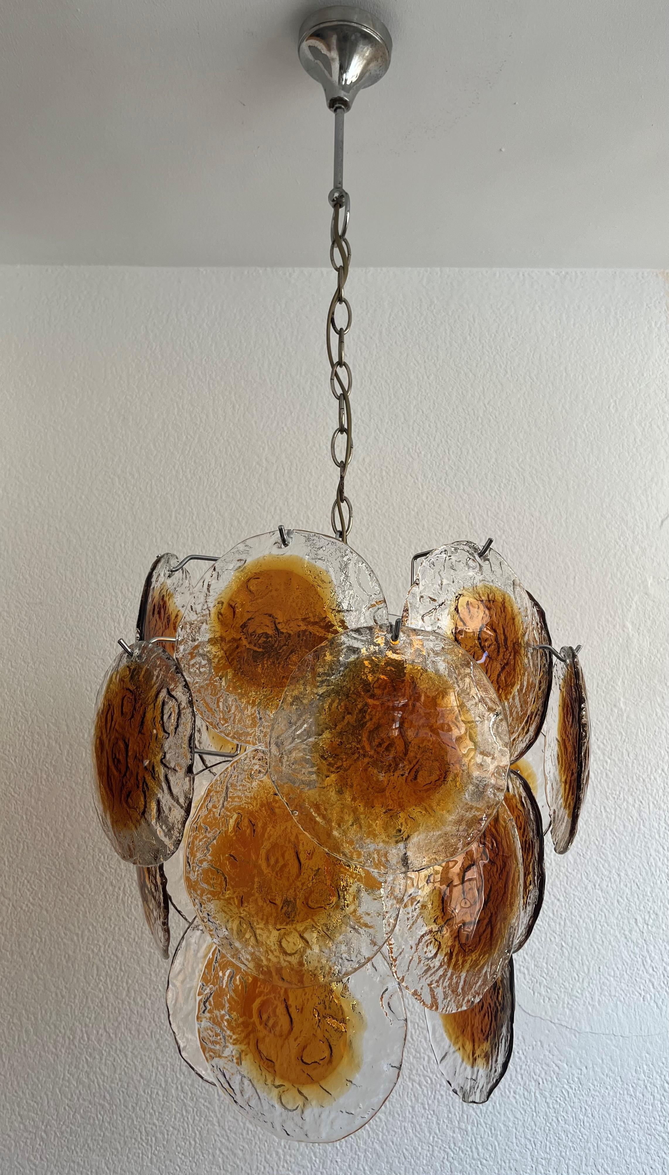Stunning Italian amber clear Murano discs Chandelier from 1970s. This fixture was designed and manufaactured during the 1970s in Italy.
This fixture is composed by 20 murano disc glasses.
This Chandelier is equipped with 6 light sockets E14. A