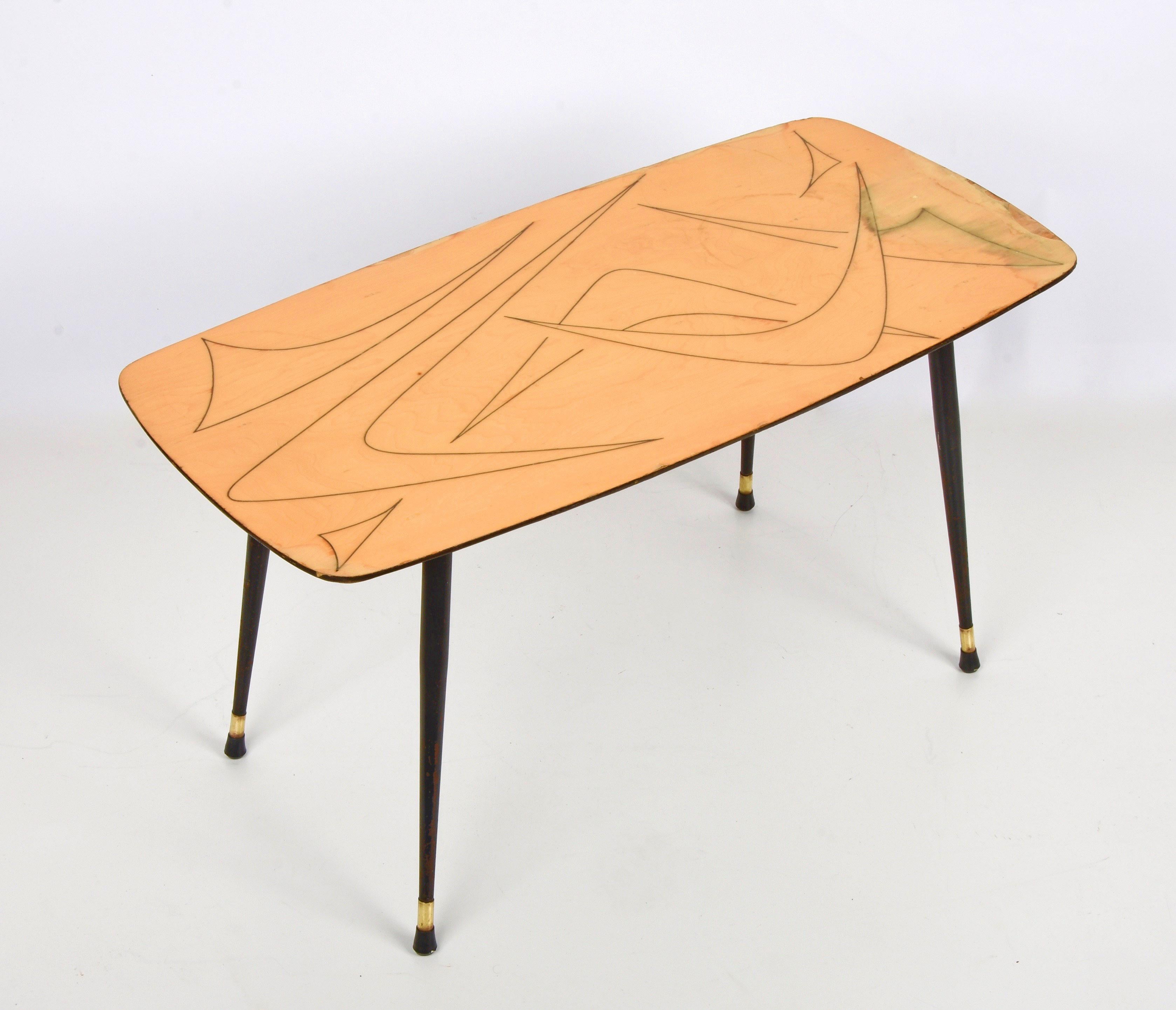 Marvellous midcentury coffee table in drawn wood, brass and black enamelled metal. This table was produced in Italy during the 1950s.

It is a rare and elegant coffee table in lacquered and yellow-painted wood, it has black metal legs with brass