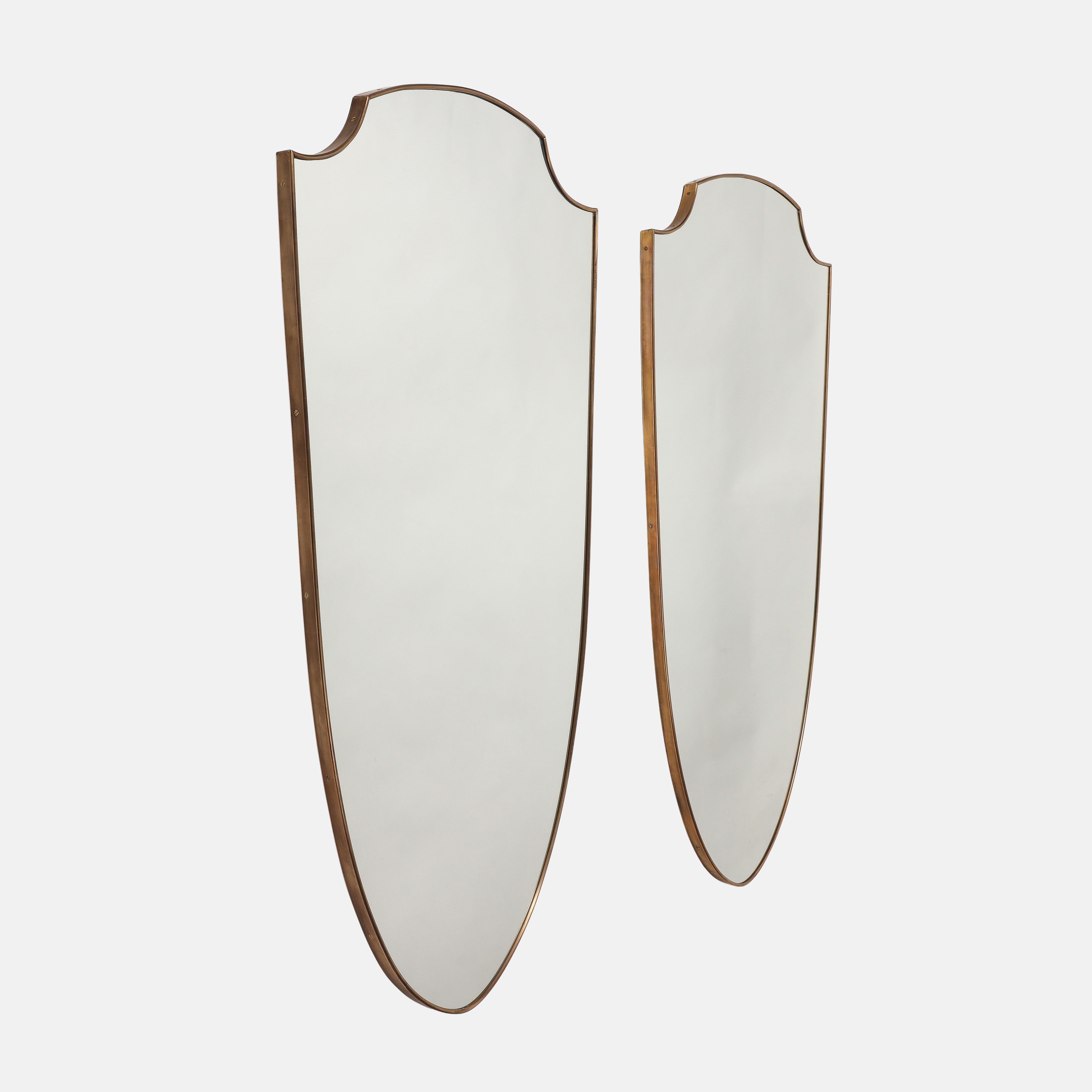 1950s Paire de miroirs en laiton en forme de bouclier avec support en bois, 1950s. Ces miroirs originaux de la période du milieu du siècle ont une belle patine riche au laiton, des courbes douces et élégantes, et des côtés effilés qui se terminent