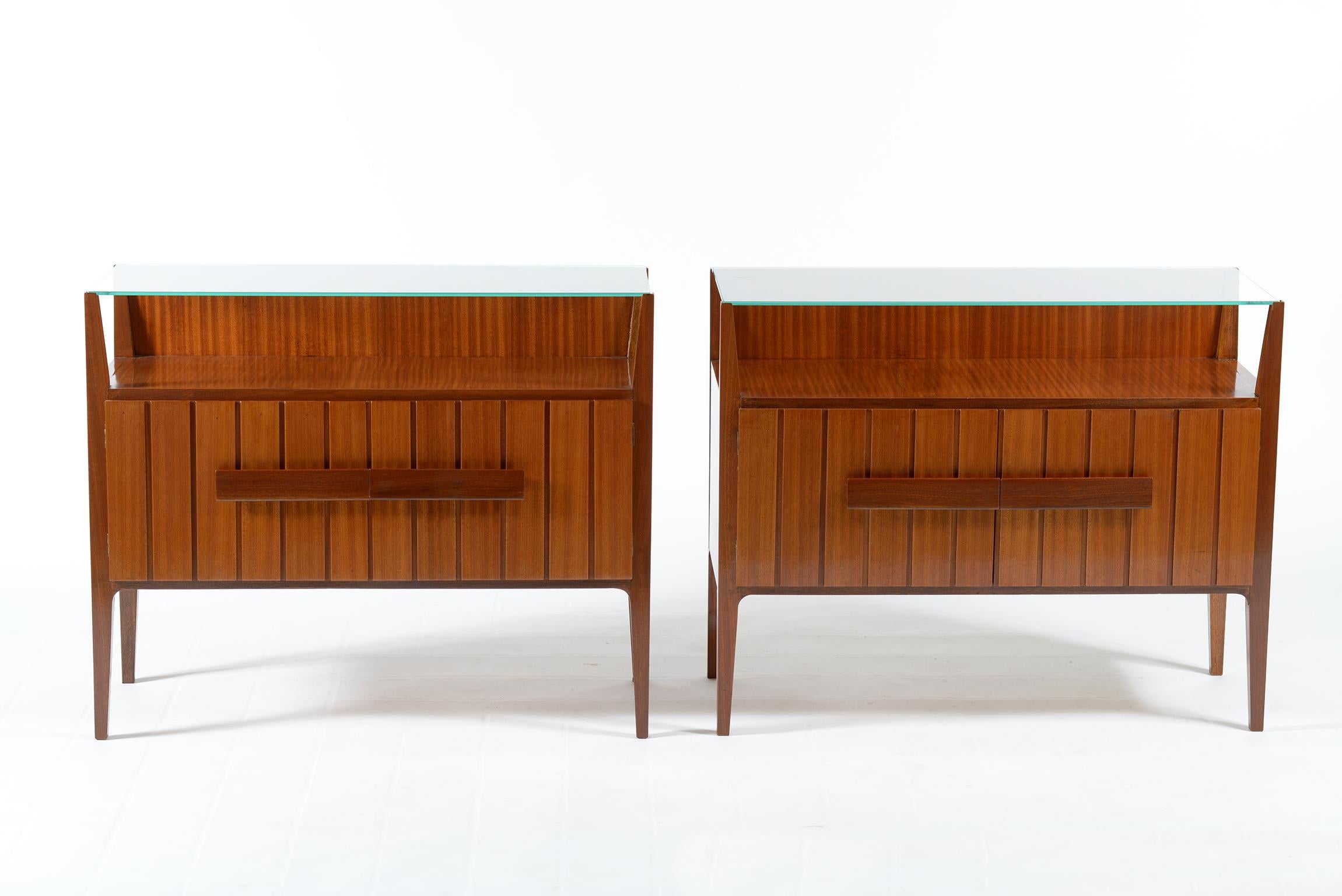 Italian midcentury two doors nightstands or side tables, sculptured solid wood handles.
Four slender legs support a glass top.
Two drawers inside,
1950s.
 