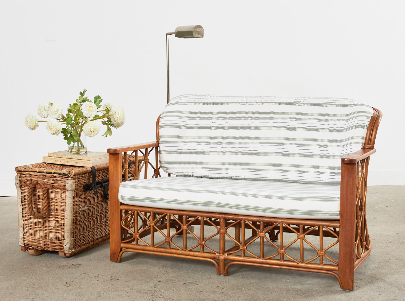 Stylish mid-century modern Italian rattan and wicker settee or love seat hand-crafted in the organic modern coastal style. The settee features a bent rattan and wood frame with decorative geometric lattice in an open fretwork design. The frame has a