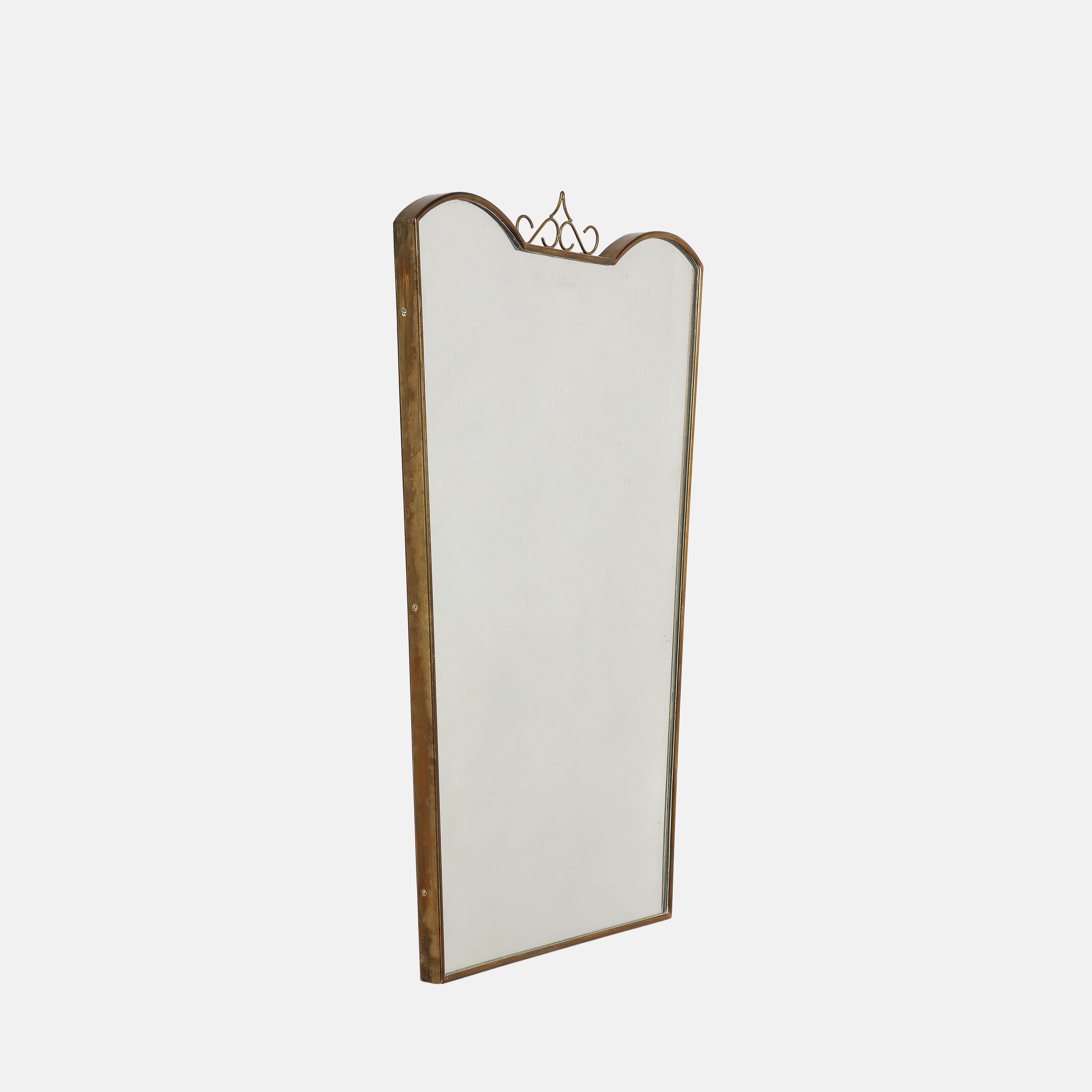 Midcentury Italian shaped brass mirror with elegant decorative brass element on central top of the frame. This lyrical brass top decoration is a fine example of the midcentury Novecento design element, which was both classical yet modernist, and was