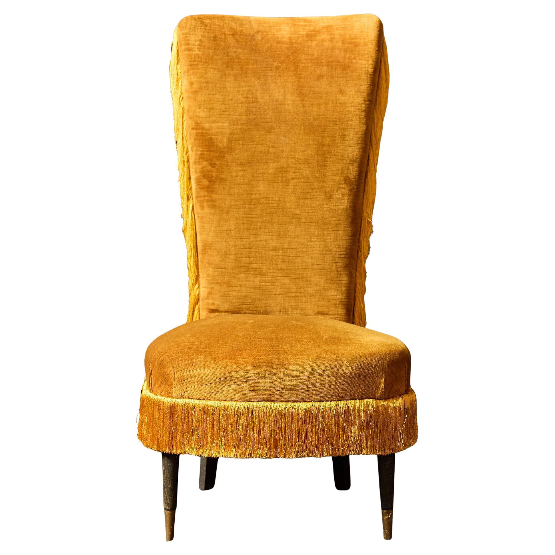 Midcentury Italian slipper chair with an elongated and flared back, plush seat with corner pleats, and raised on black lacquered legs and brass capped feet. The accent chair is upholstered in a vintage gold velvet and is accentuated with silk fringe