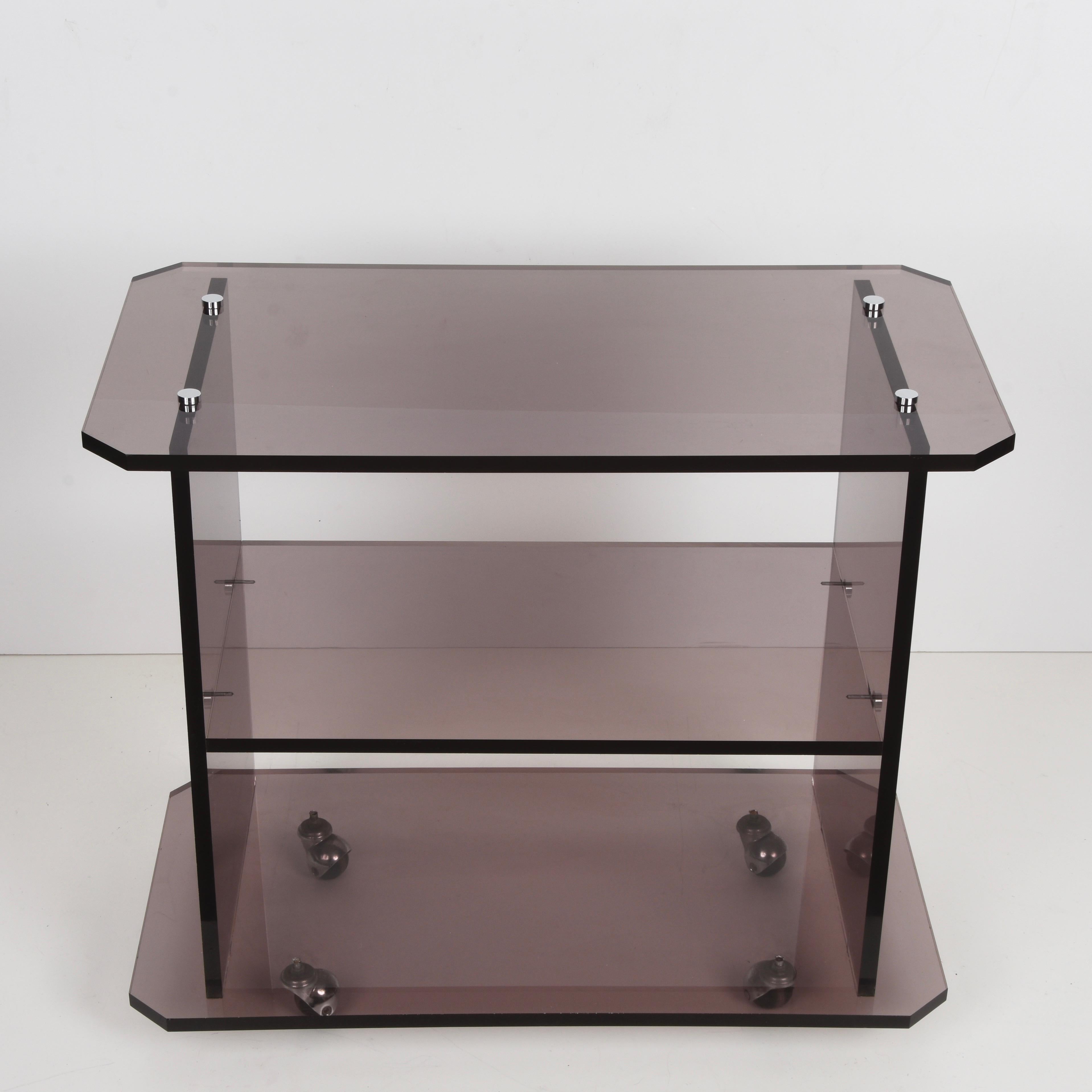 Elegant midcentury service trolley in smoked plexiglass. This magnificent item is in the style of Willy Rizzo and was produced in Italy during the 1980s.

This piece is unique because of the synthetic lines and the material, that allows exploring