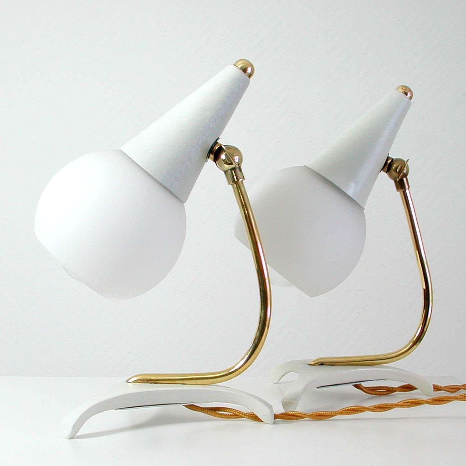 This set of 2 table lamps was manufactured in Italy in the 1950s. 

The lamps are made of white lacquered metal and brass and have got adjustable opaline glass globe lampshades.
The lamps have been polished, rewired and can be used in US, Europe