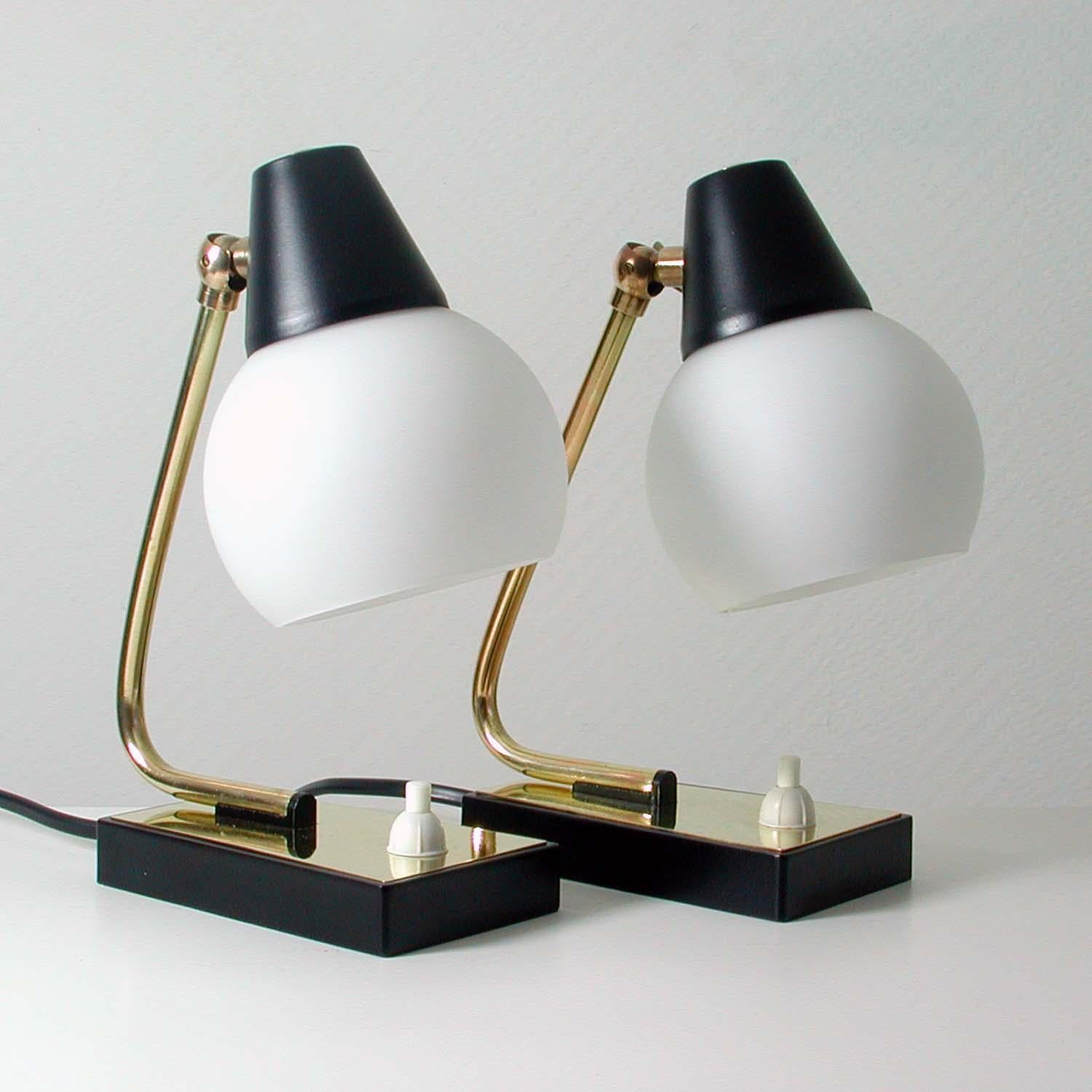 This set of 2 table lamps was manufactured in Italy in the 1950s. 
The lamps are made of black lacquered metal and brass and have got adjustable opaline glass globe lampshades.
The lamps have been polished, rewired and can be used in US, Europe