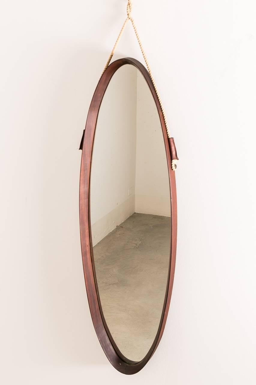 Midcentury oval wall mirror designed in the 1950s and originates from Italy. The frame is made from teak and it features a visible rope for hanging.