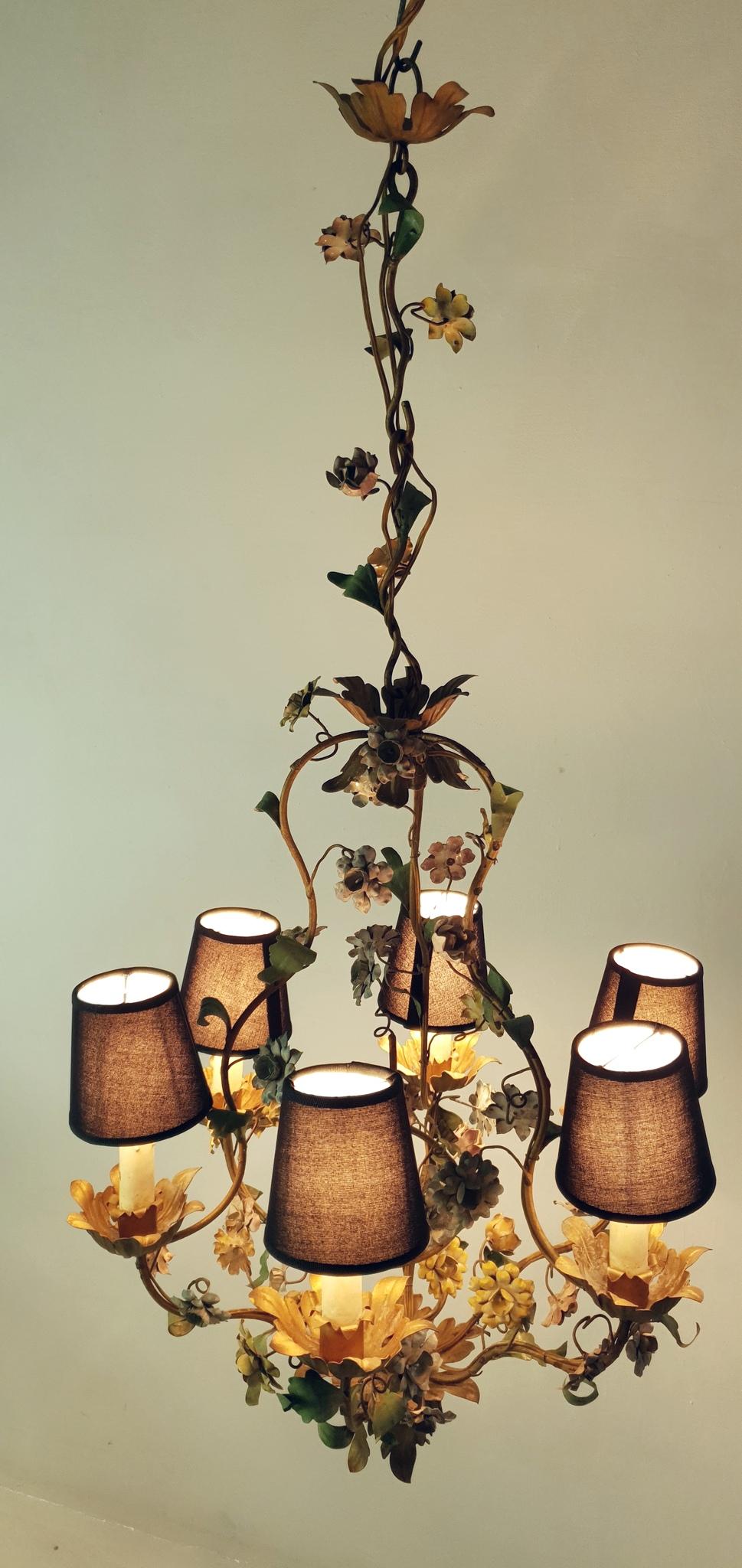 Chandelier from the 1950s in iron and painted with a natural vintage patina. It has six candle lights surrounded with flowers and leaves in different shapes and colors. The lightbulbs used are Edison e14 which are found both in Europe and the United