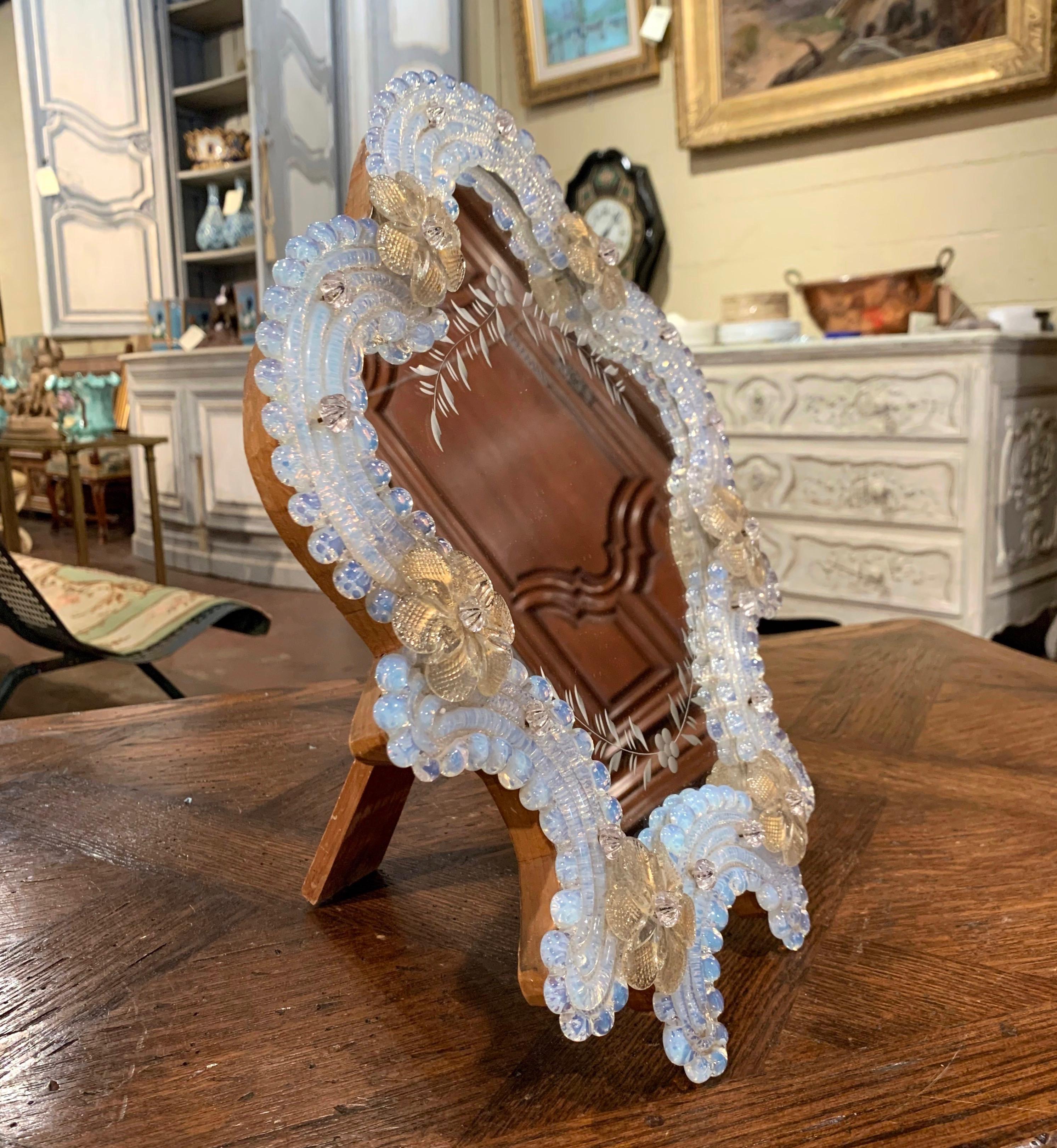 This elegant table mirror was created in Murano, Italy circa 1960, the free standing vanity mirror with wooden back is surrounded with handmade clear and gold Bohemian flowers. The decorative mirror is in excellent condition and further embellished