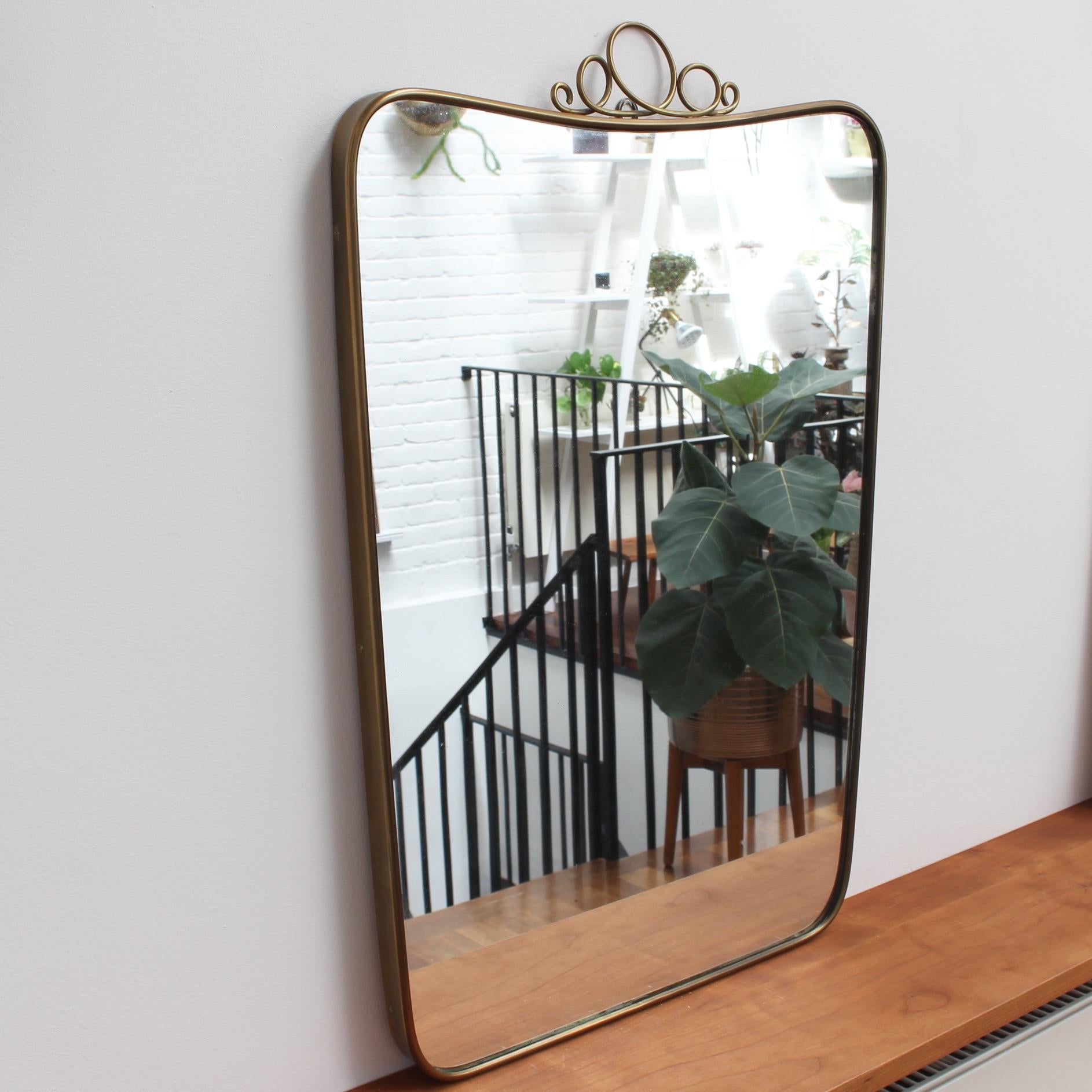 Midcentury Italian wall mirror with brass frame, circa 1950s by Gio Ponti (1891-1979). The mirror is classically shaped, and with its distinctive top-fitted flourish, a clear sign of an original design by Gio Ponti. The mirror is in very good