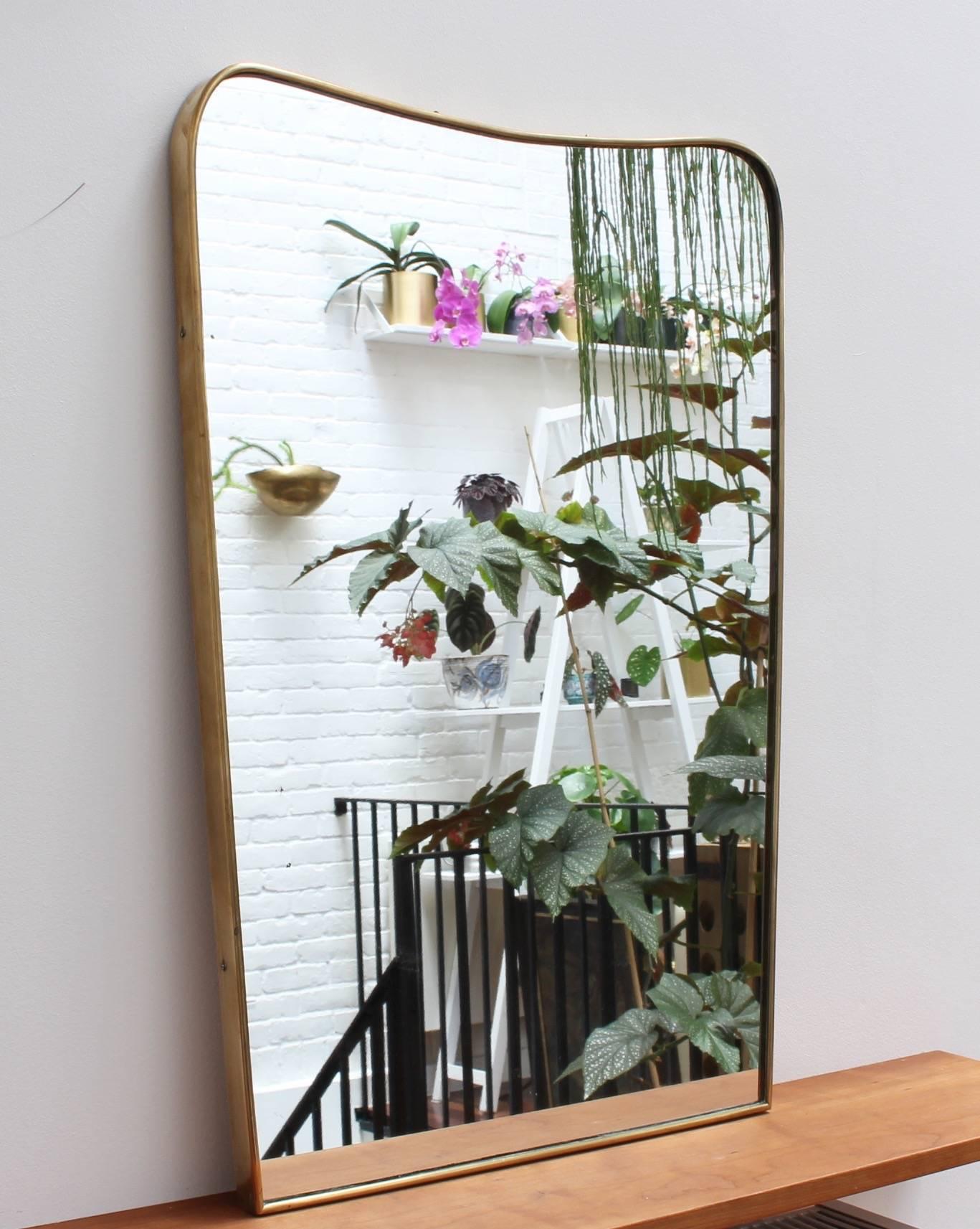 Midcentury Italian wall mirror with brass frame, circa 1950s. The mirror is in the form of a shield, or more whimsically, shaped like a slice of bread. Still classically elegant and distinctive in a modern Gio Ponti style. This piece is in very good